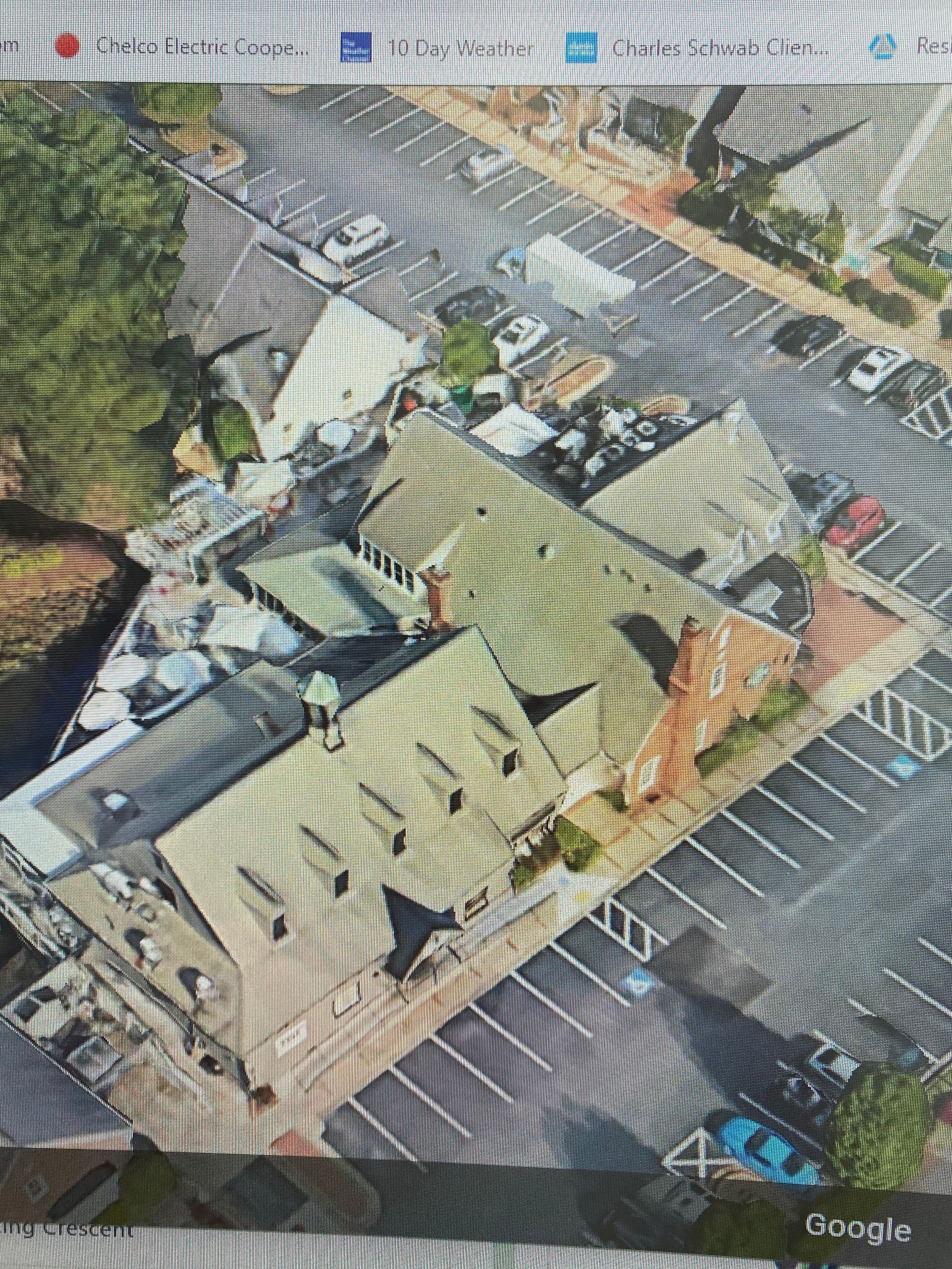 Aerial view of a building with a gray roof and a parking lot. Some cars are present.