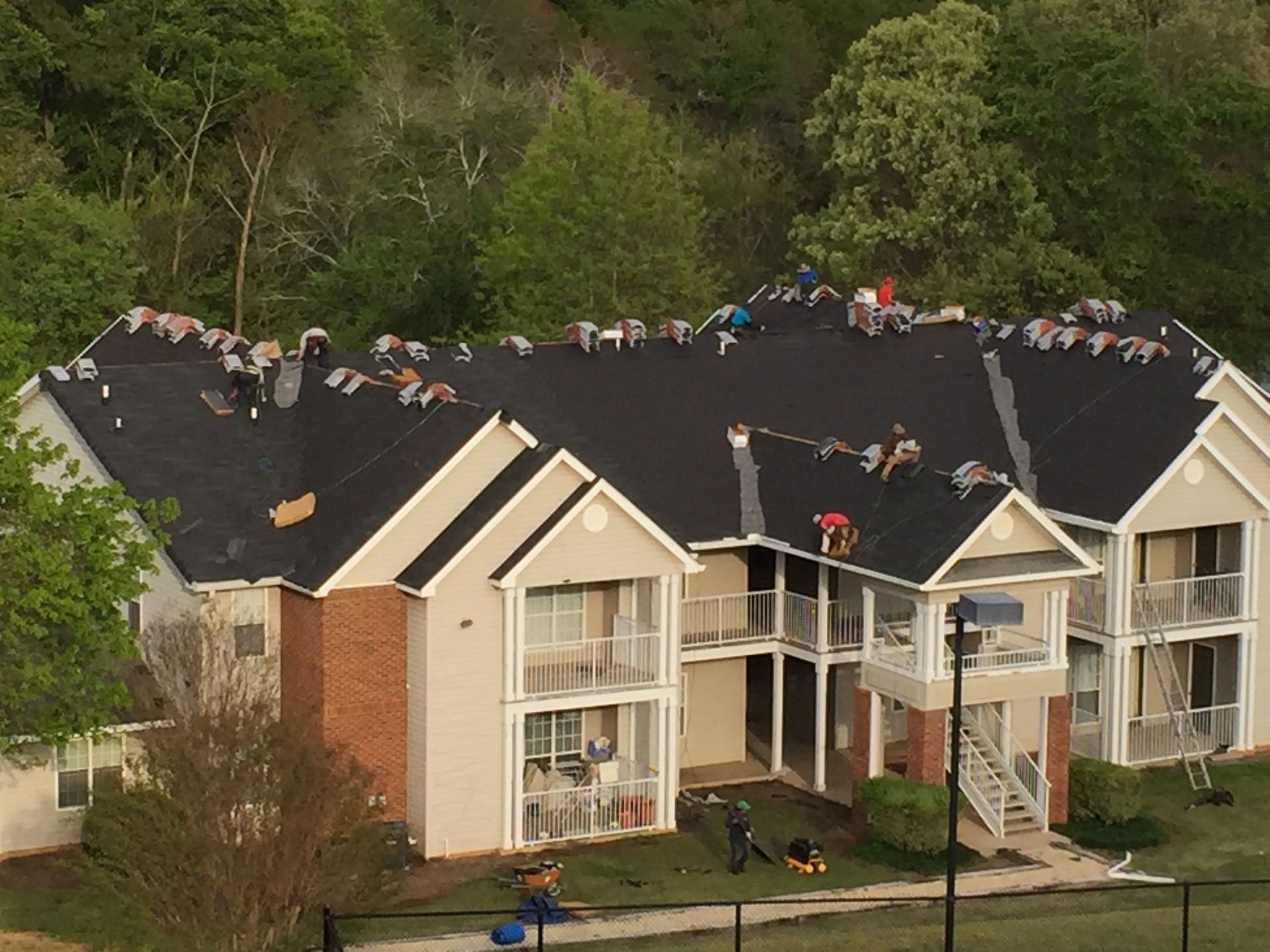 Workers replace a black shingle roof on a multi-story apartment building.