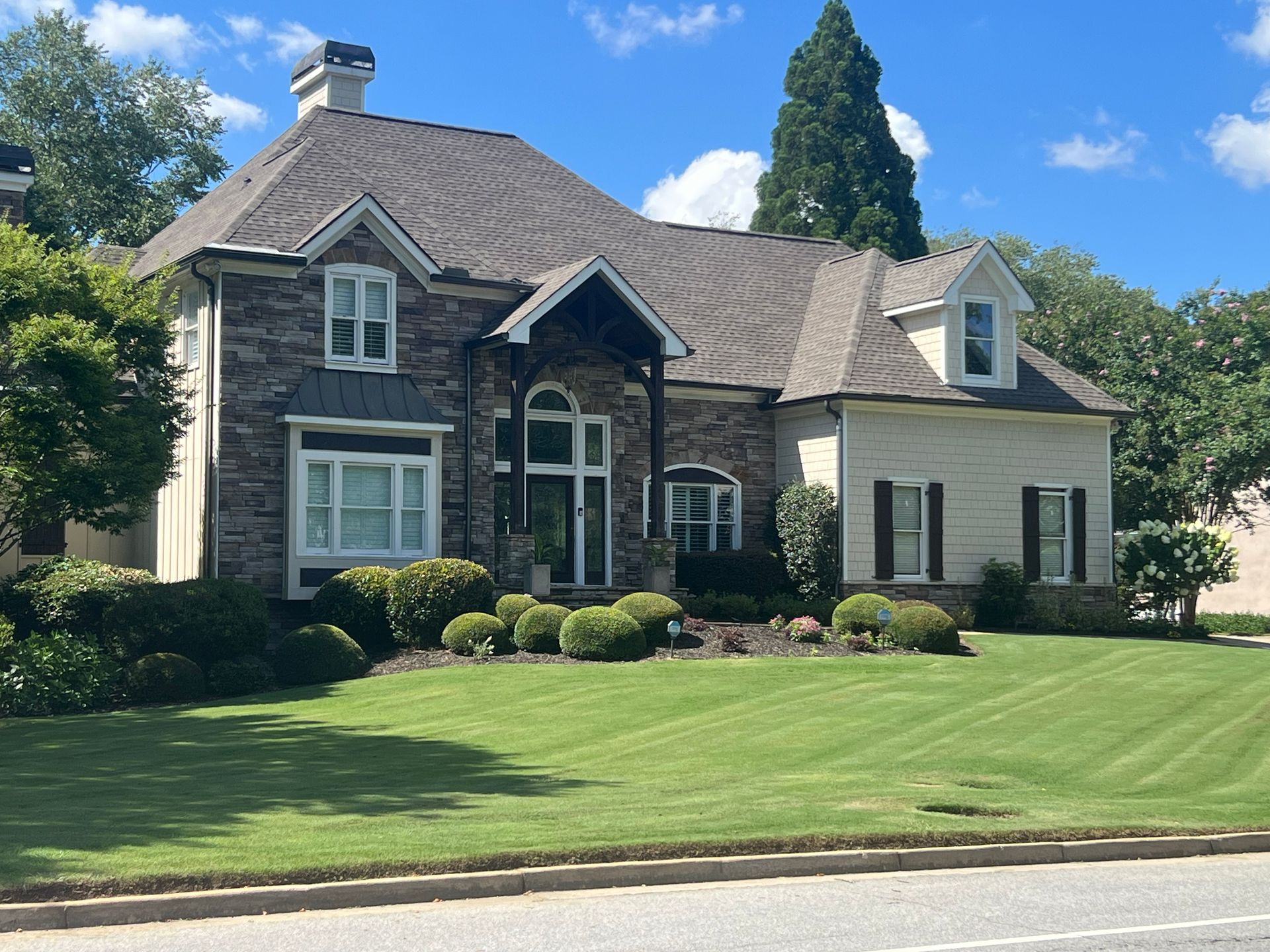 A two-story house with a stone facade, beige siding, and manicured lawn.