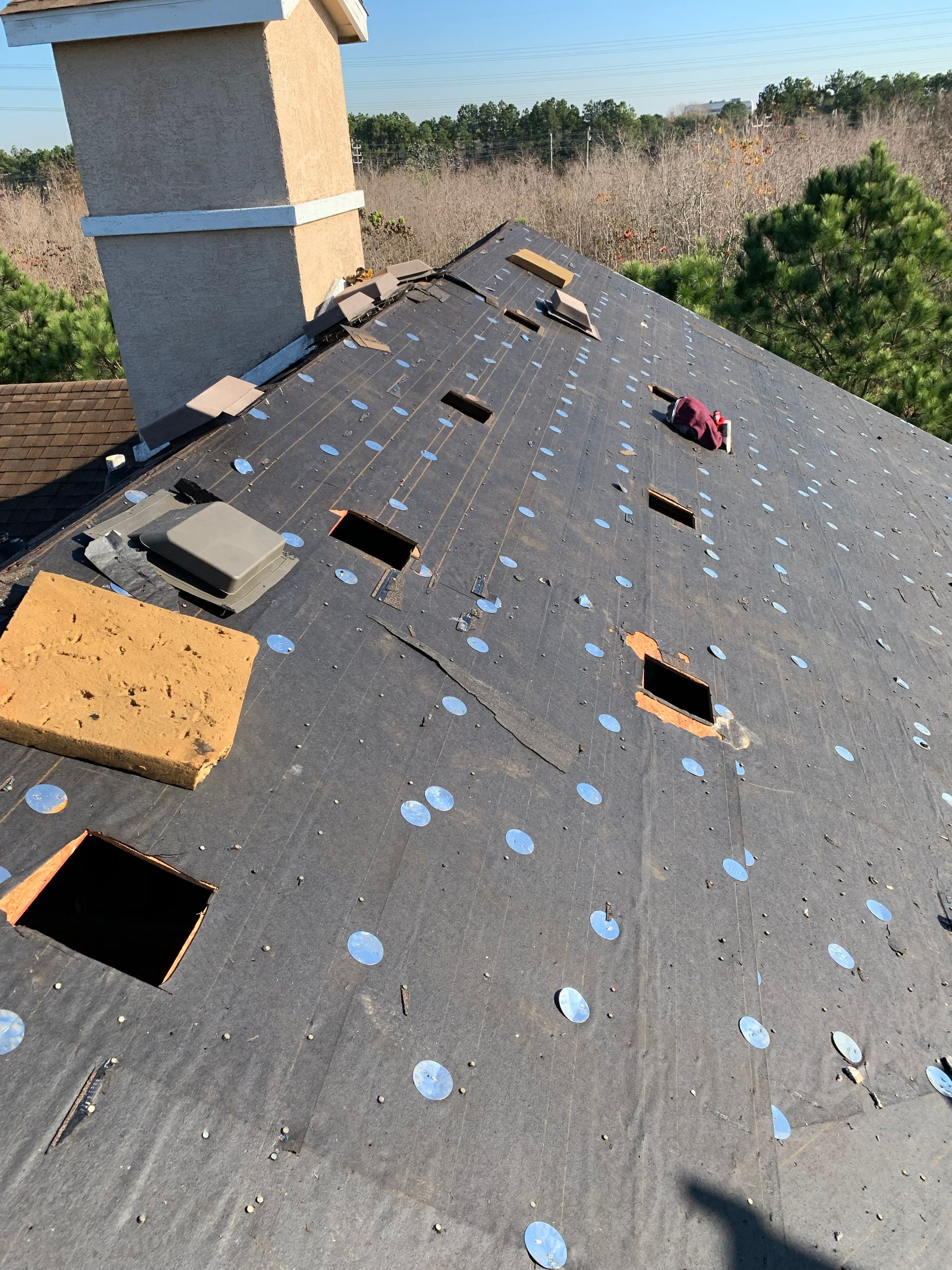 Roof under repair with holes, exposed underlayment, and chimney.