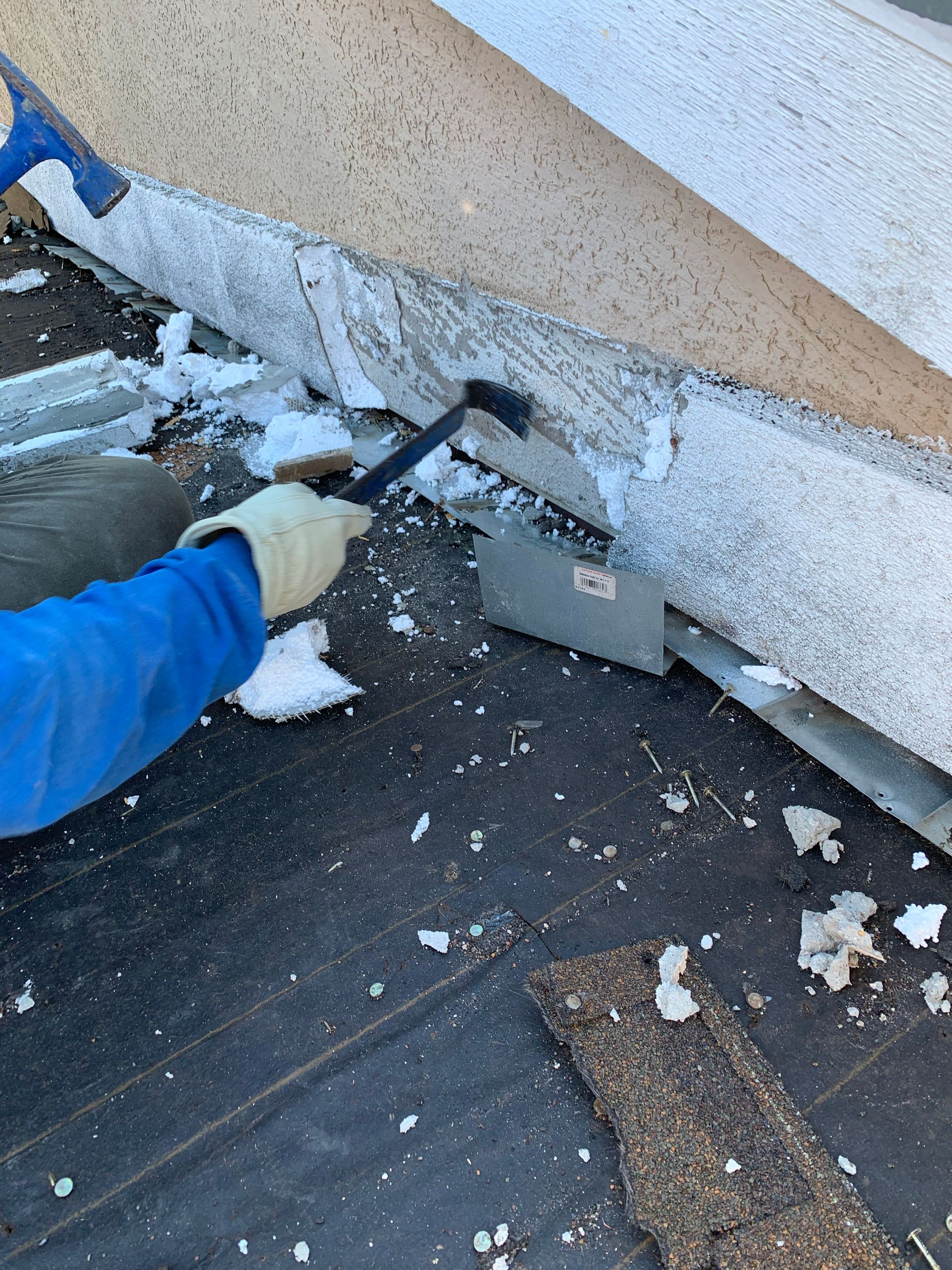 Person wearing gloves uses a tool to remove material from a building's roof edge.