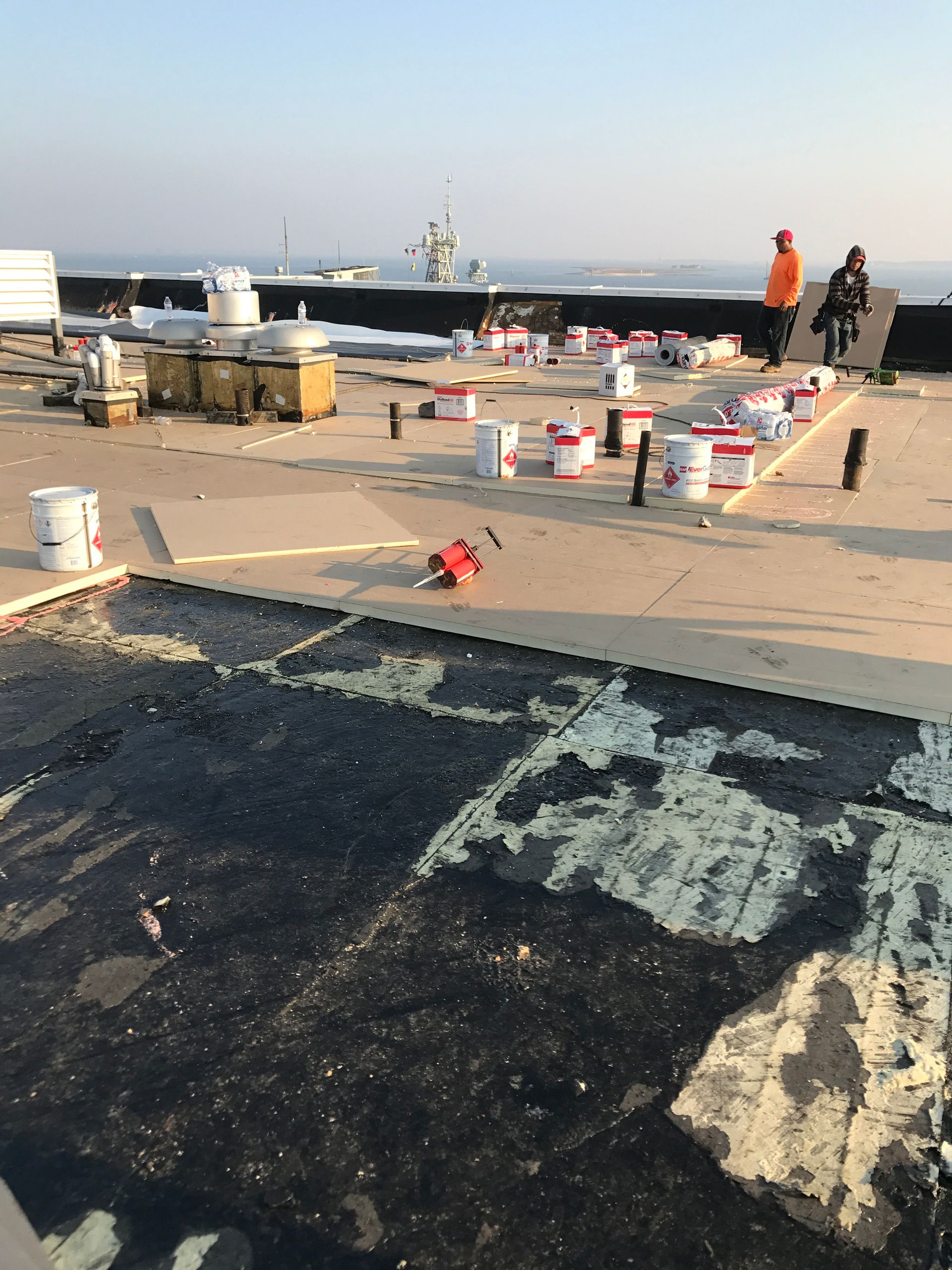 Roof repair with buckets, tools, and workers; water in background.