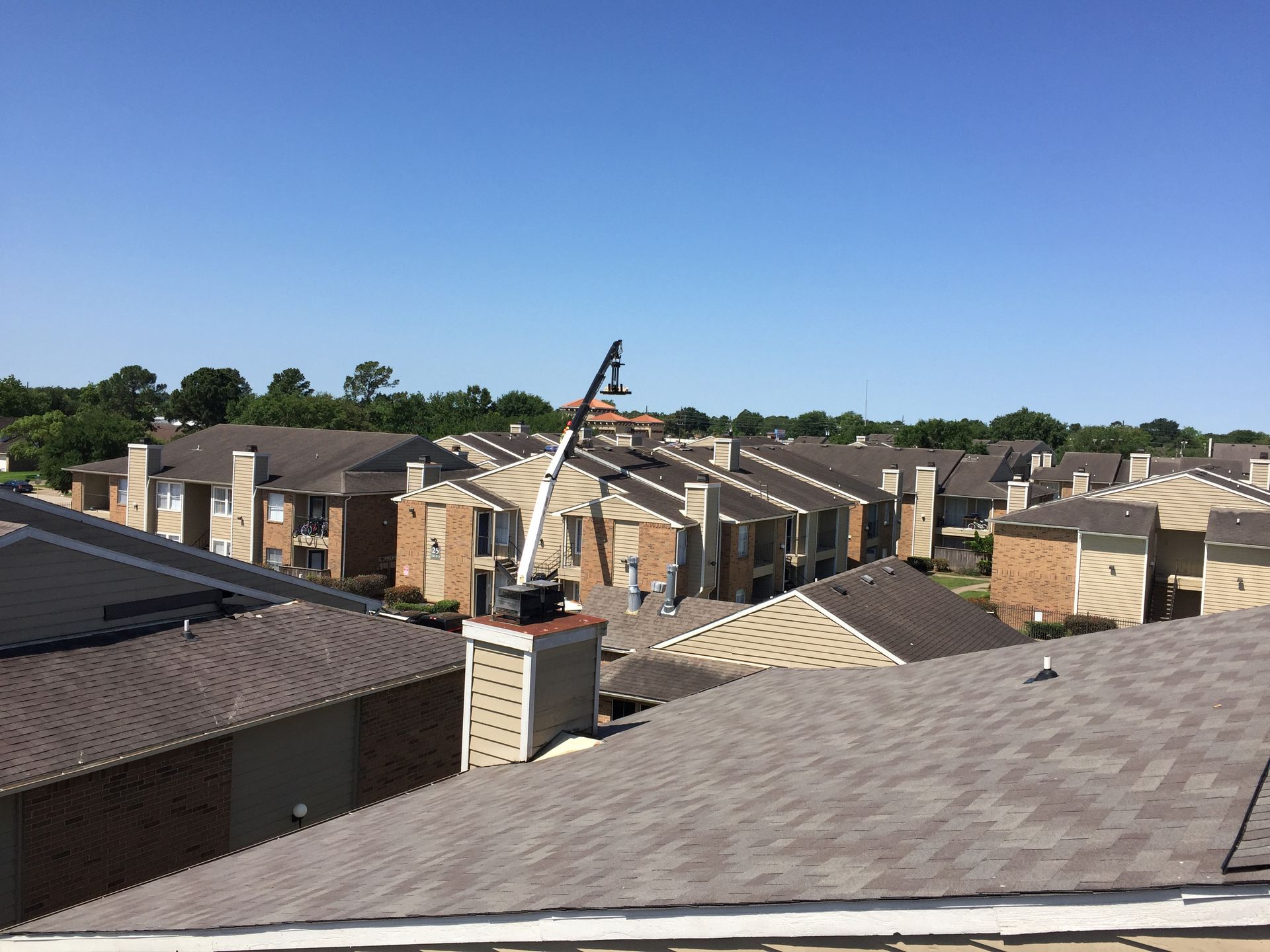 Apartment rooftops with a cherry picker extending towards a chimney under a clear blue sky.