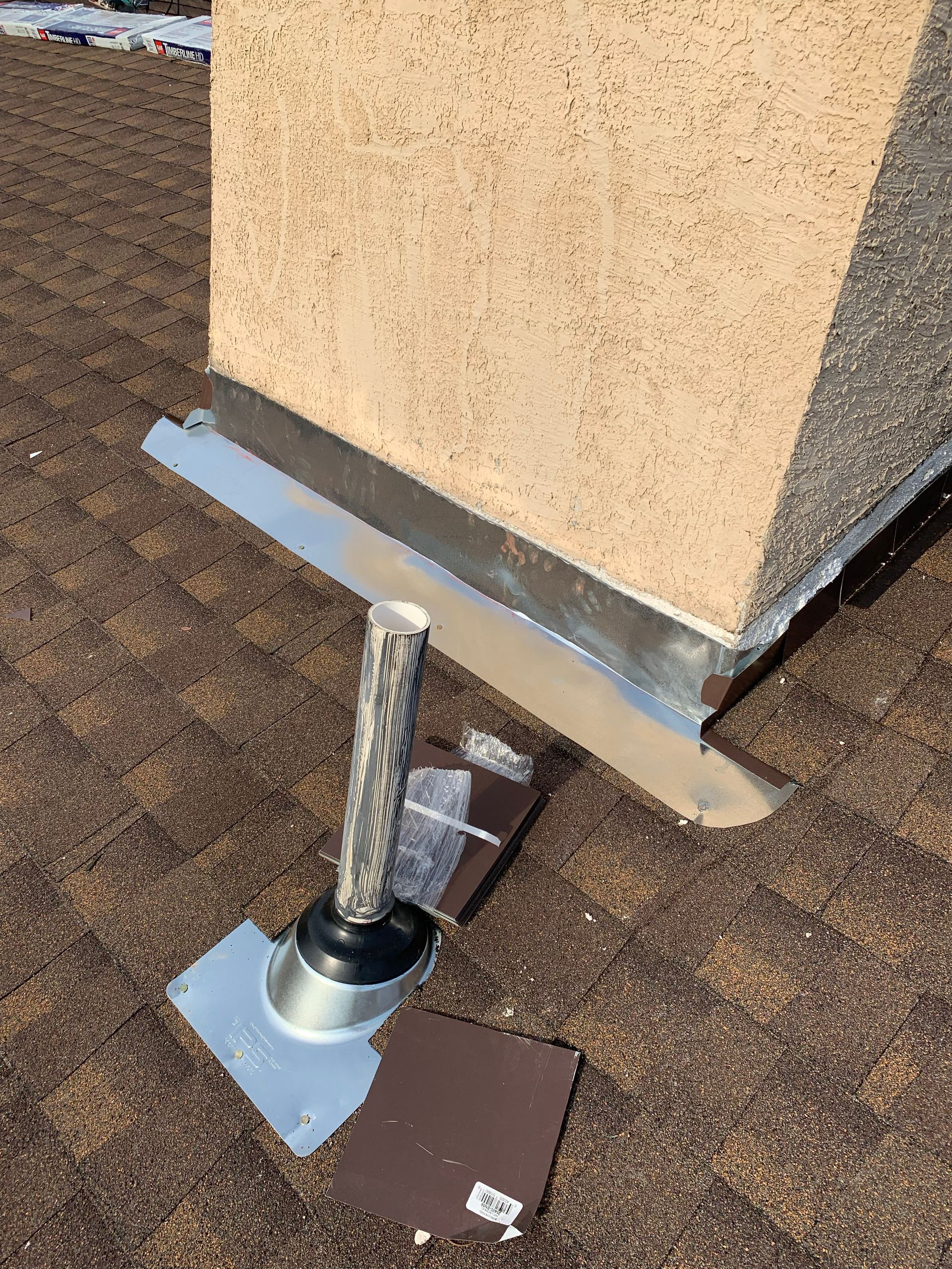 Chimney with metal flashing on a brown shingle roof, pipe with rubber boot.