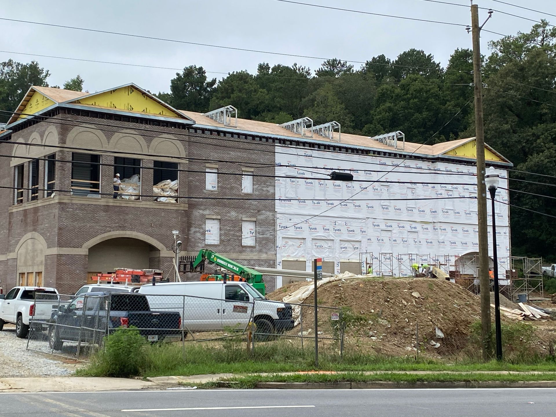 Construction site: building with brick facade and white siding. Trucks and equipment are present.