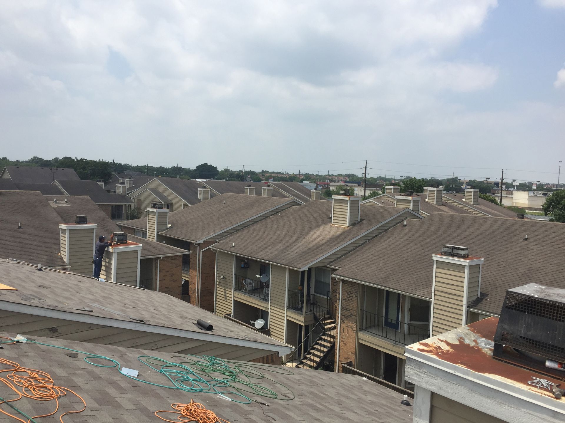 Rooftop view of apartment buildings with brown roofs under a cloudy sky.