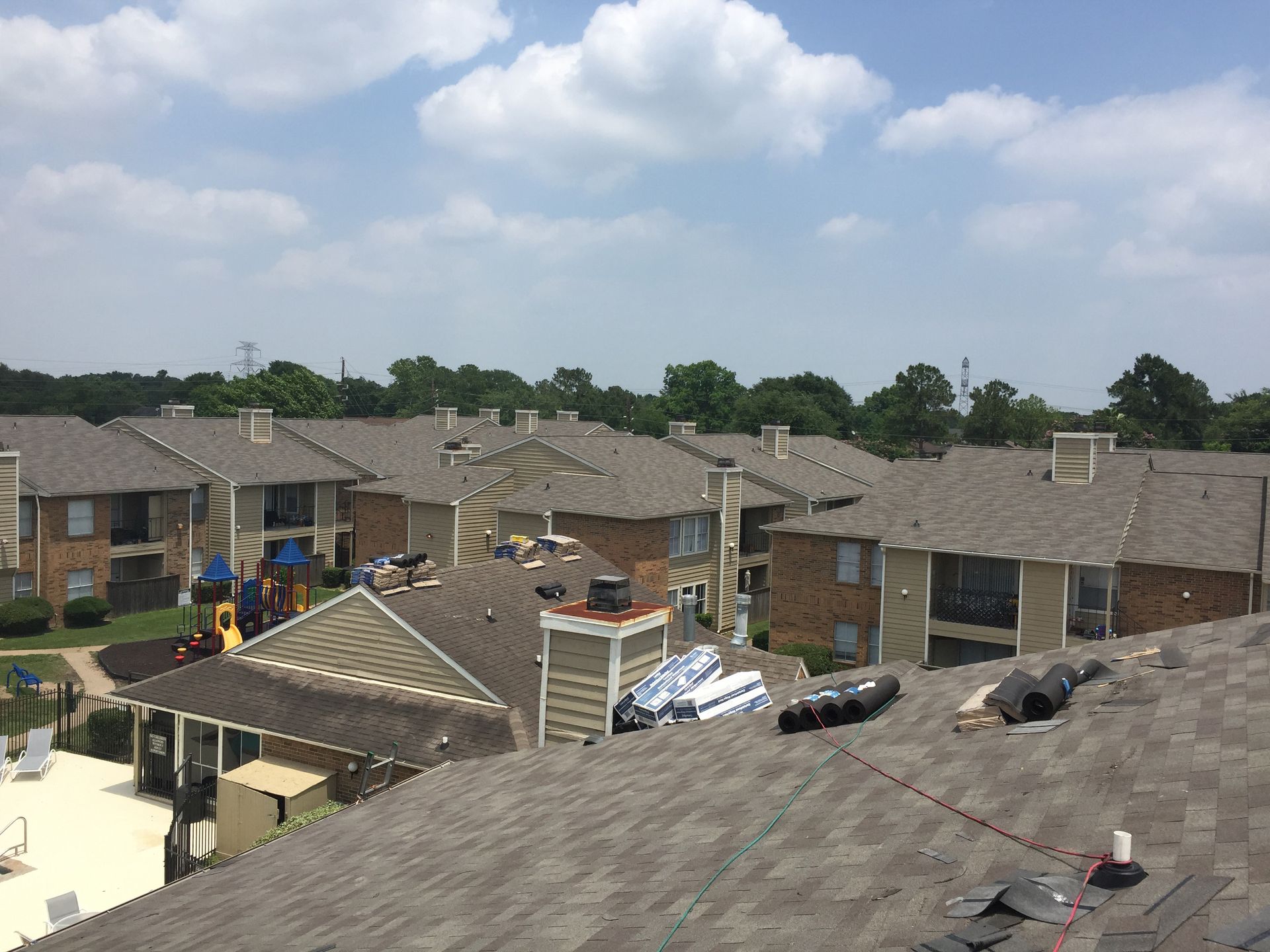 Apartment complex rooftops with construction materials visible, on a sunny day.