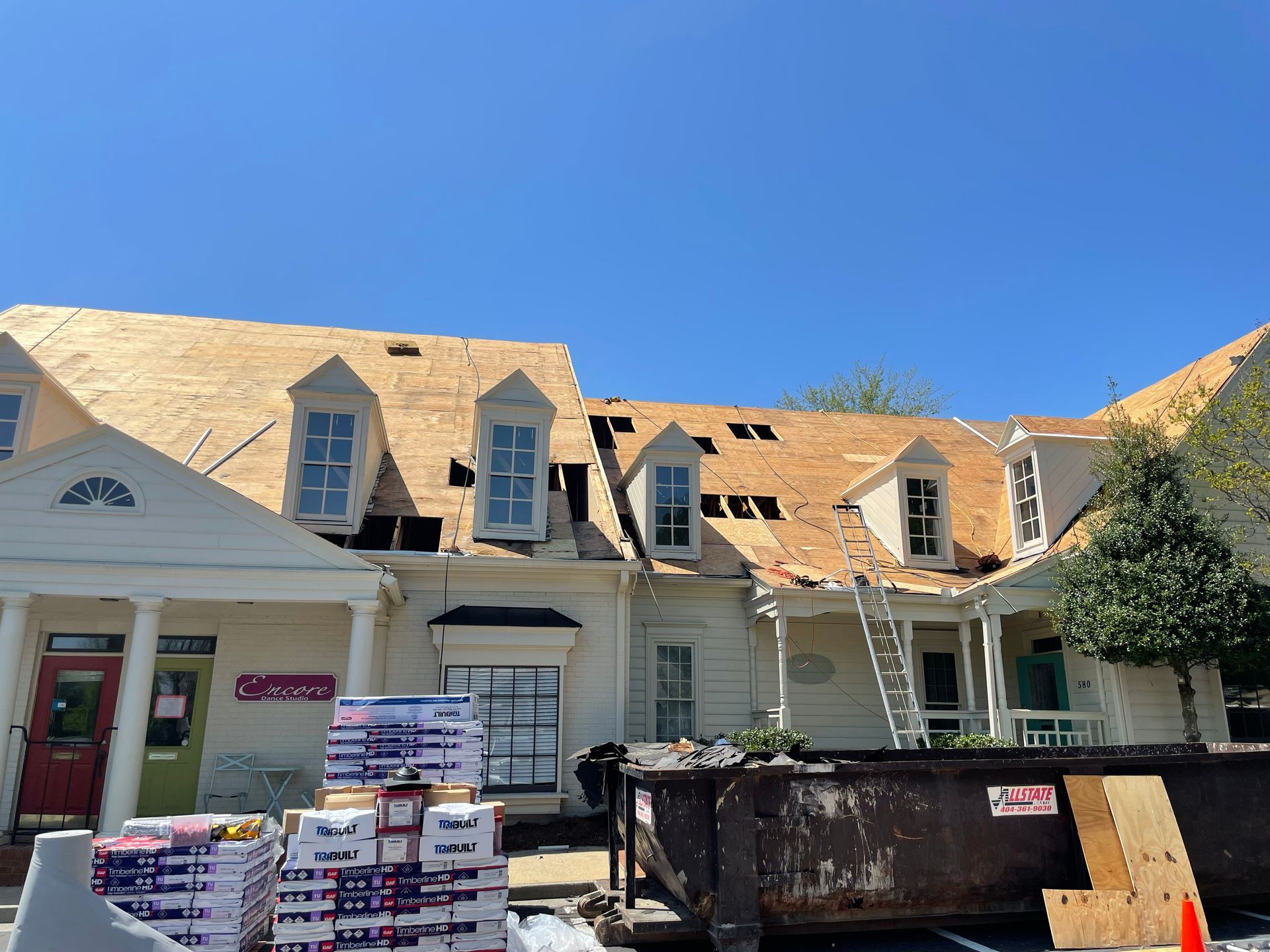 Building with roof partially under construction, several dormers, clear sky, materials on ground.