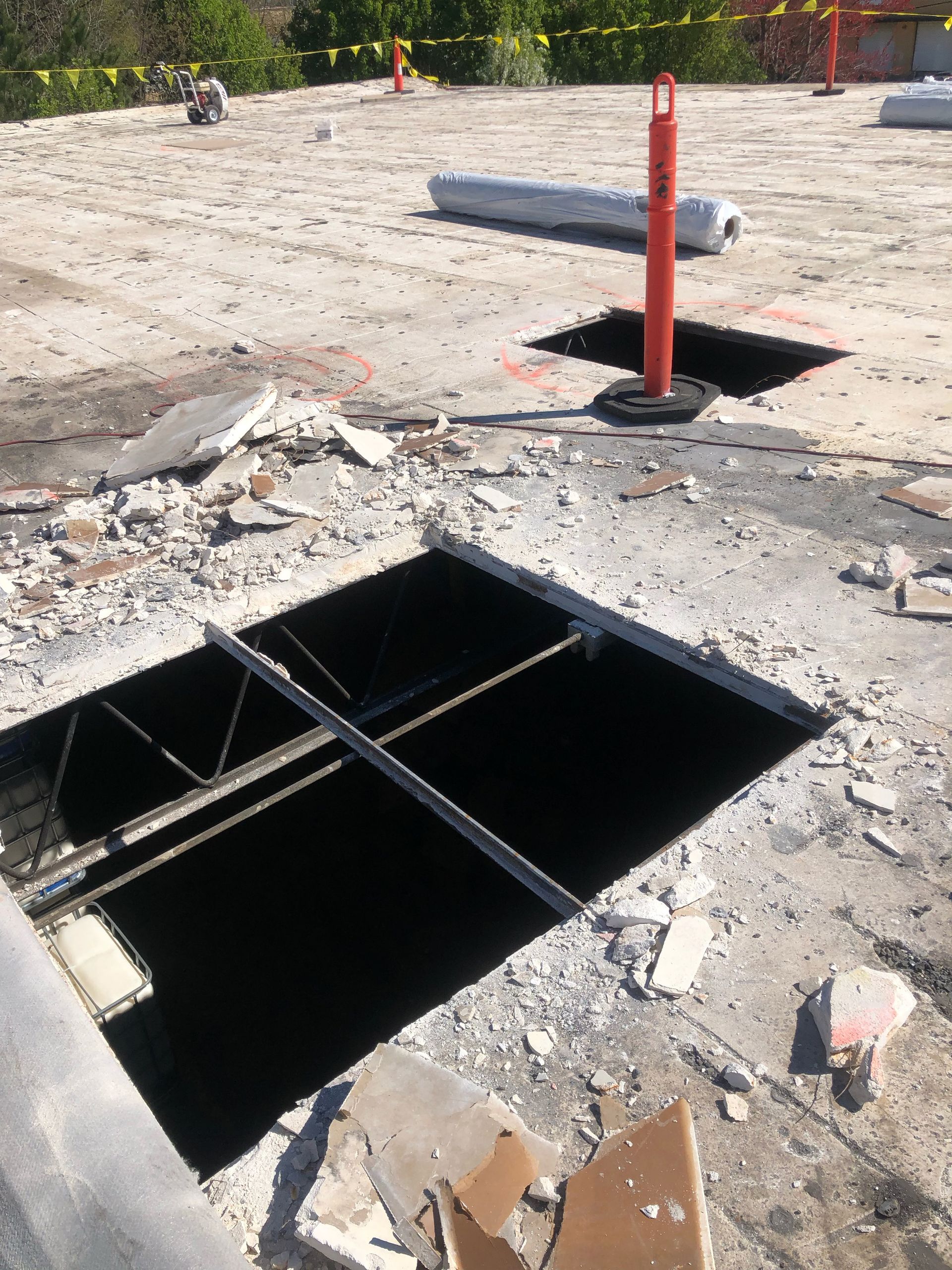 Construction site with two open holes in a concrete surface. A warning cone is placed near one hole.