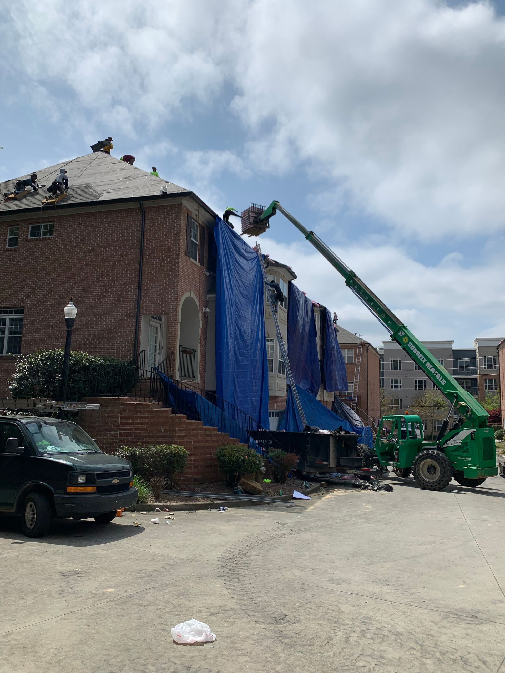 Brick building with damaged roof covered in blue tarp, being worked on with a green boom lift.