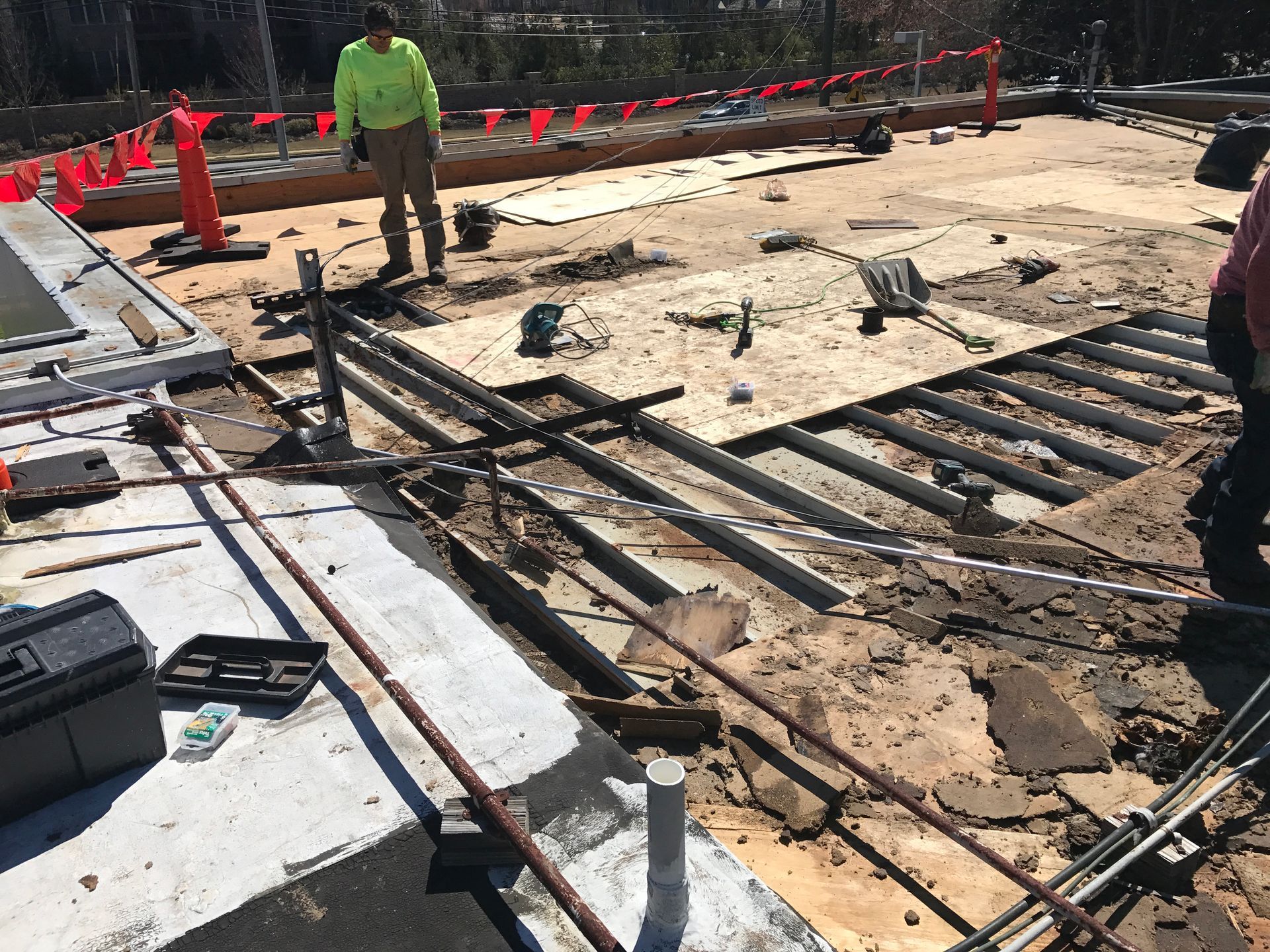 Construction site: workers on a partially demolished roof, surrounded by debris, tools, and pipes.