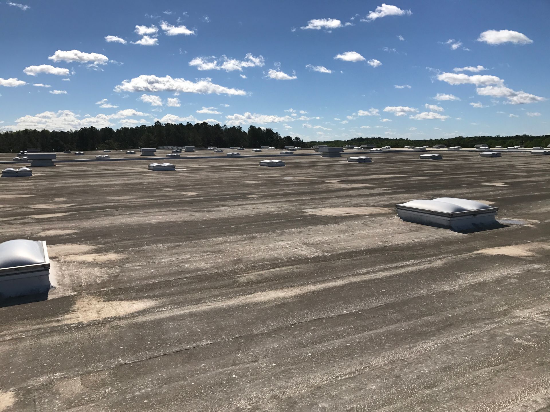 Flat roof covered in gravel with numerous rectangular vents under a blue sky.