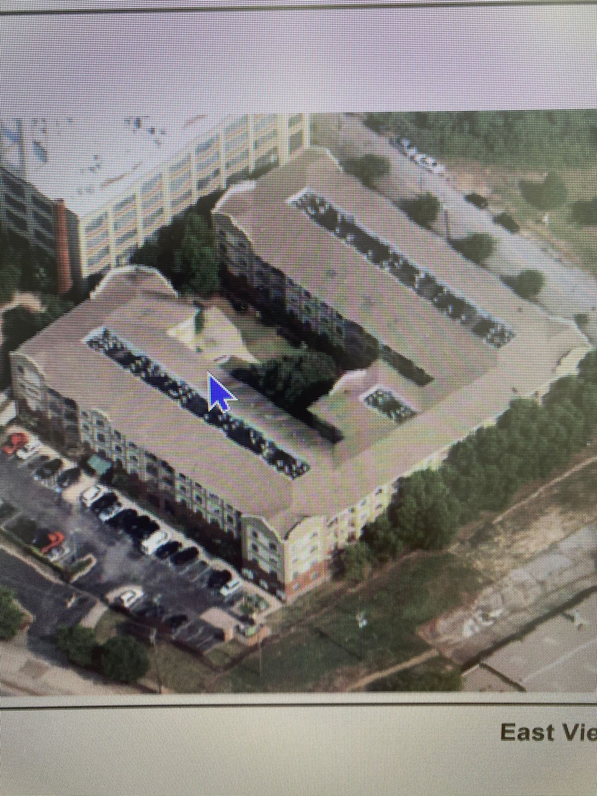 Aerial view of a rectangular building with three large, dark parallel sections. Cars are parked to the left.