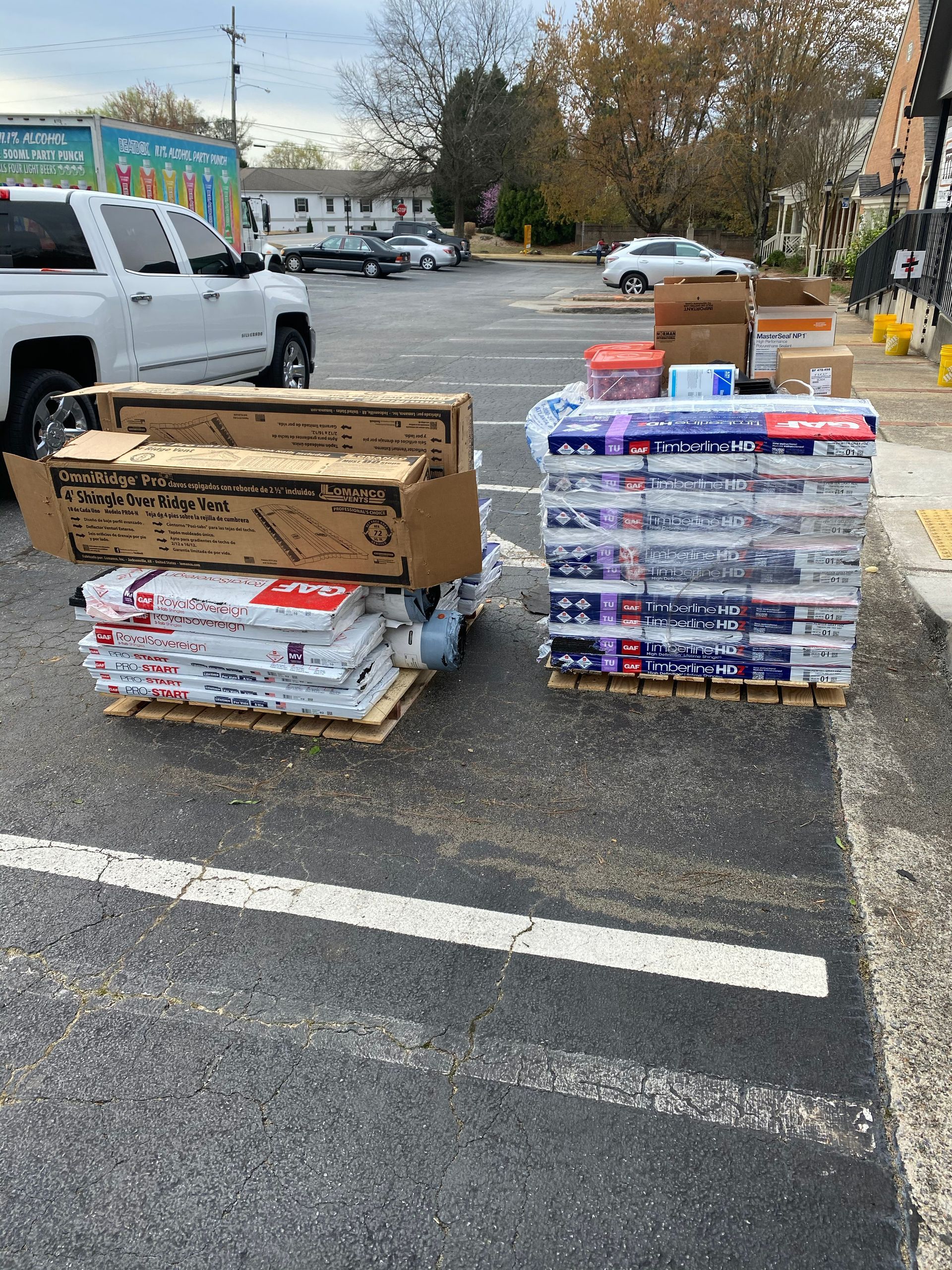 Two pallets of packaged items, including paper, boxes, and other supplies, sit in a parking lot.