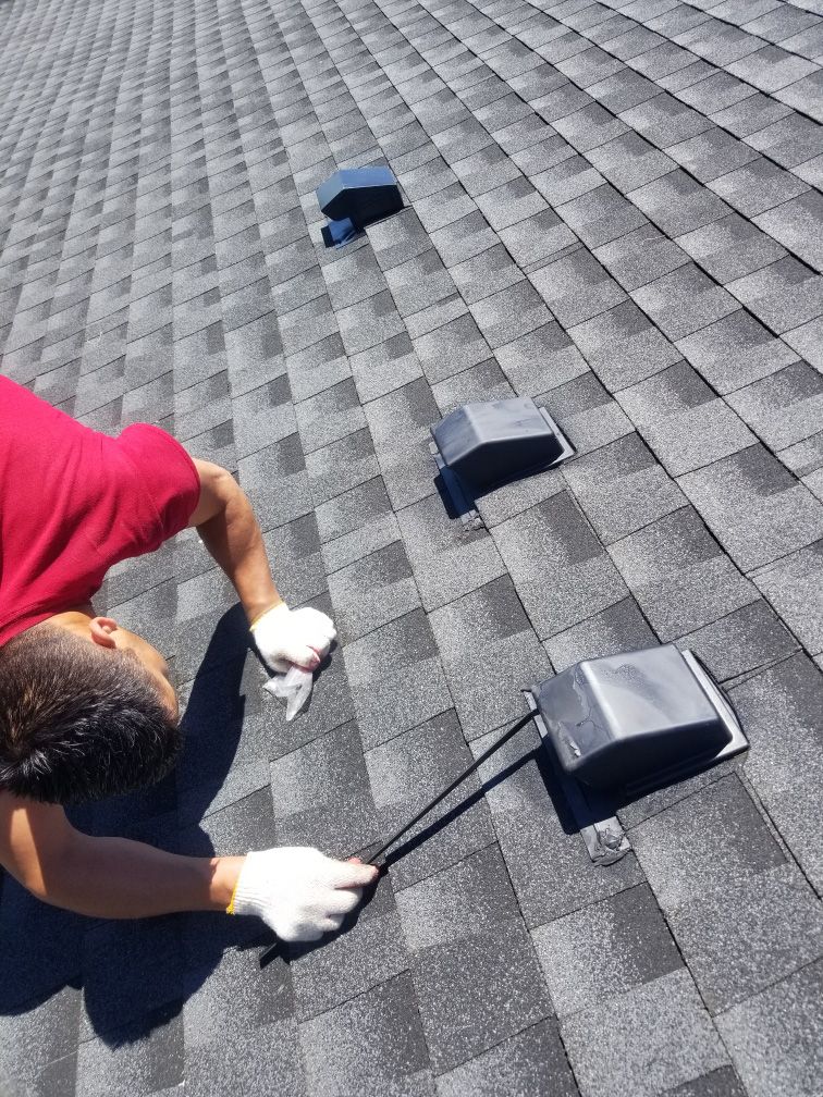 Person wearing gloves on a shingled roof, examining a vent.