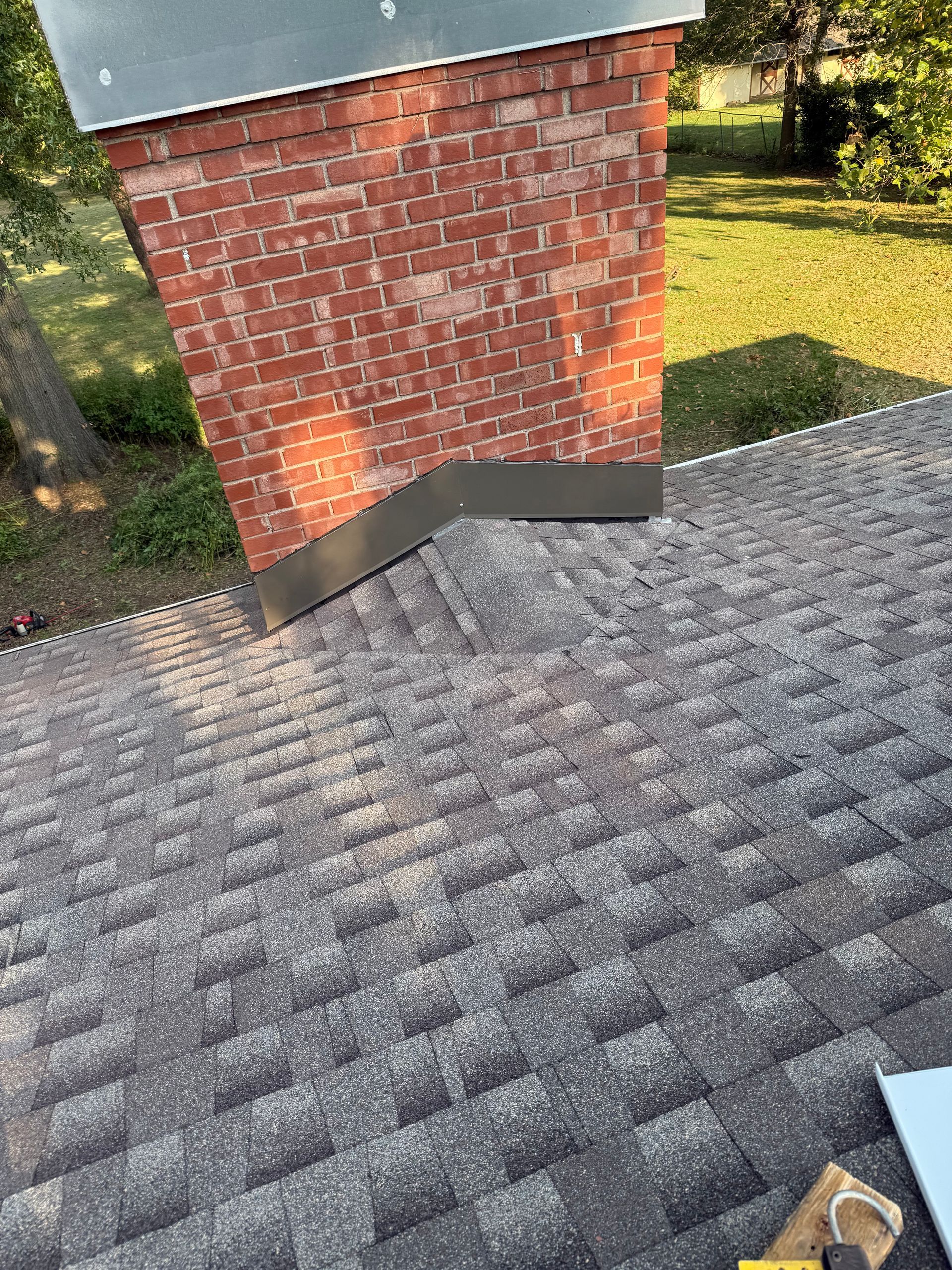 Brick chimney leaning on a gray shingled roof, outdoors.