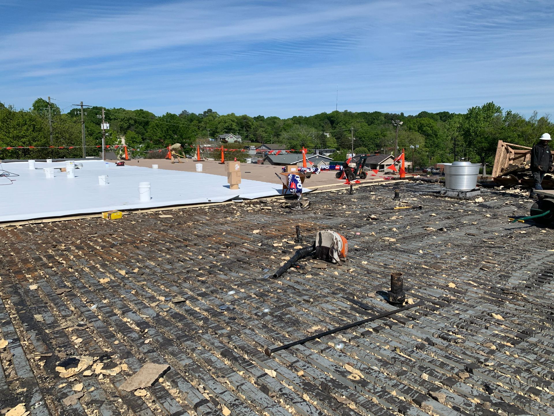 Roofing work on a building: Old roof exposed, new white membrane installed, workers visible, bright blue sky.