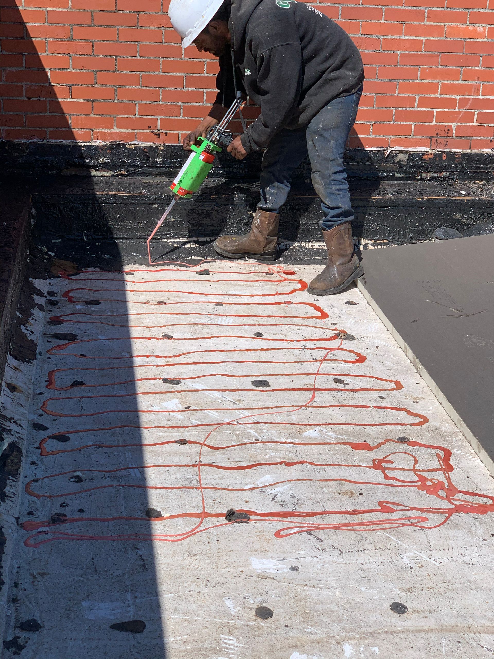 Person applying sealant on a concrete surface of a rooftop. Red sealant lines are visible.