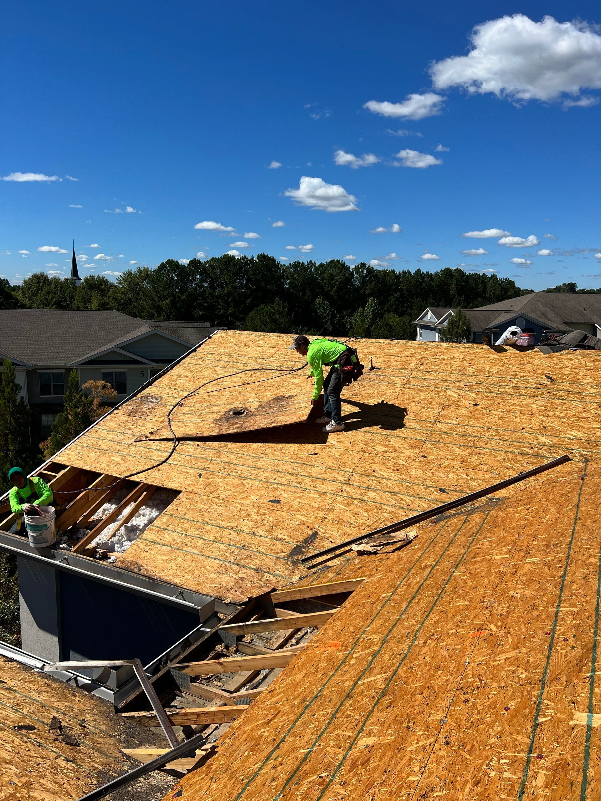 Roofers in neon green vests work on a house roof on a sunny day.