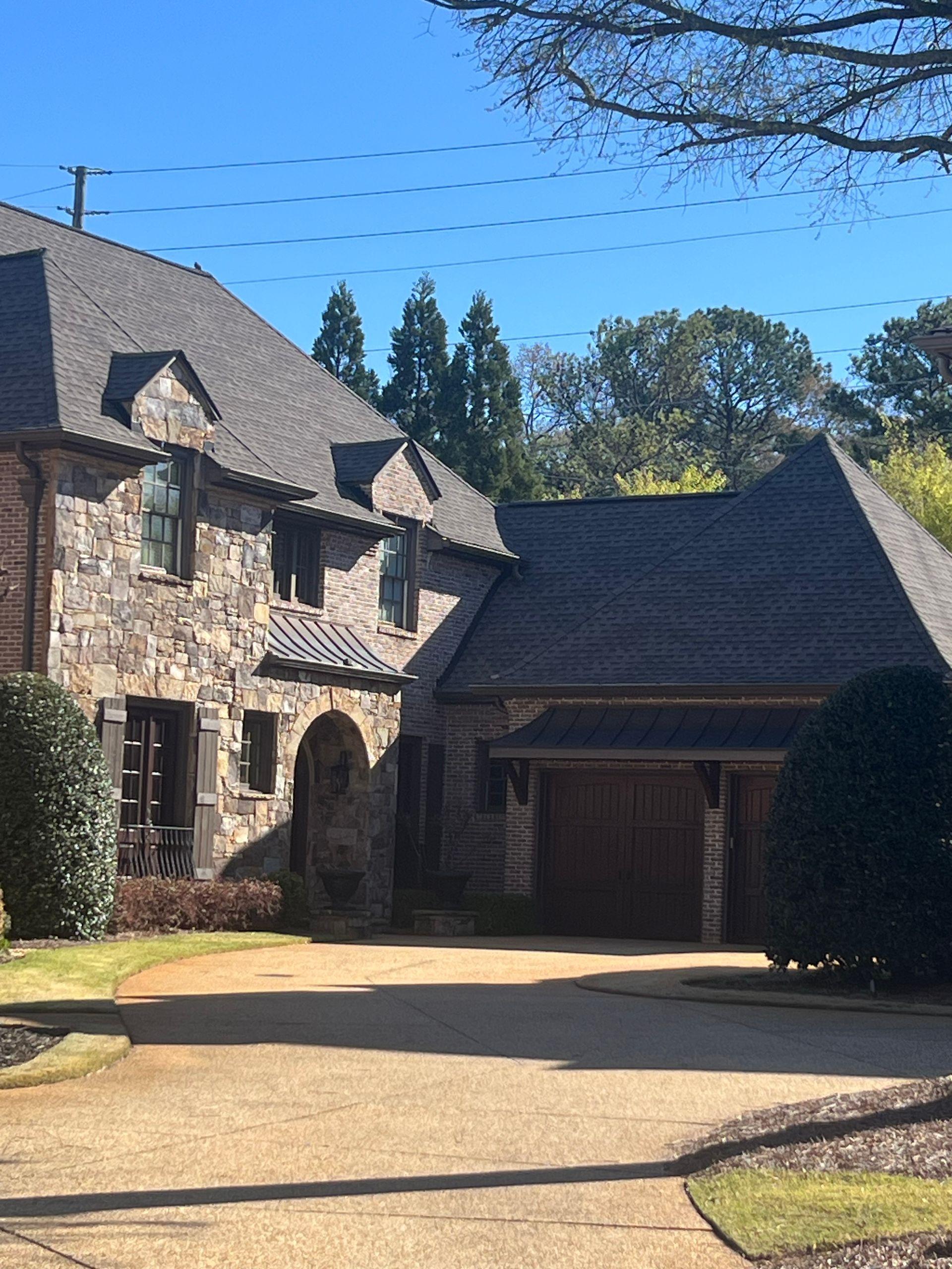 Stone house with dark roof and attached garage; long driveway leads toward the entrance.