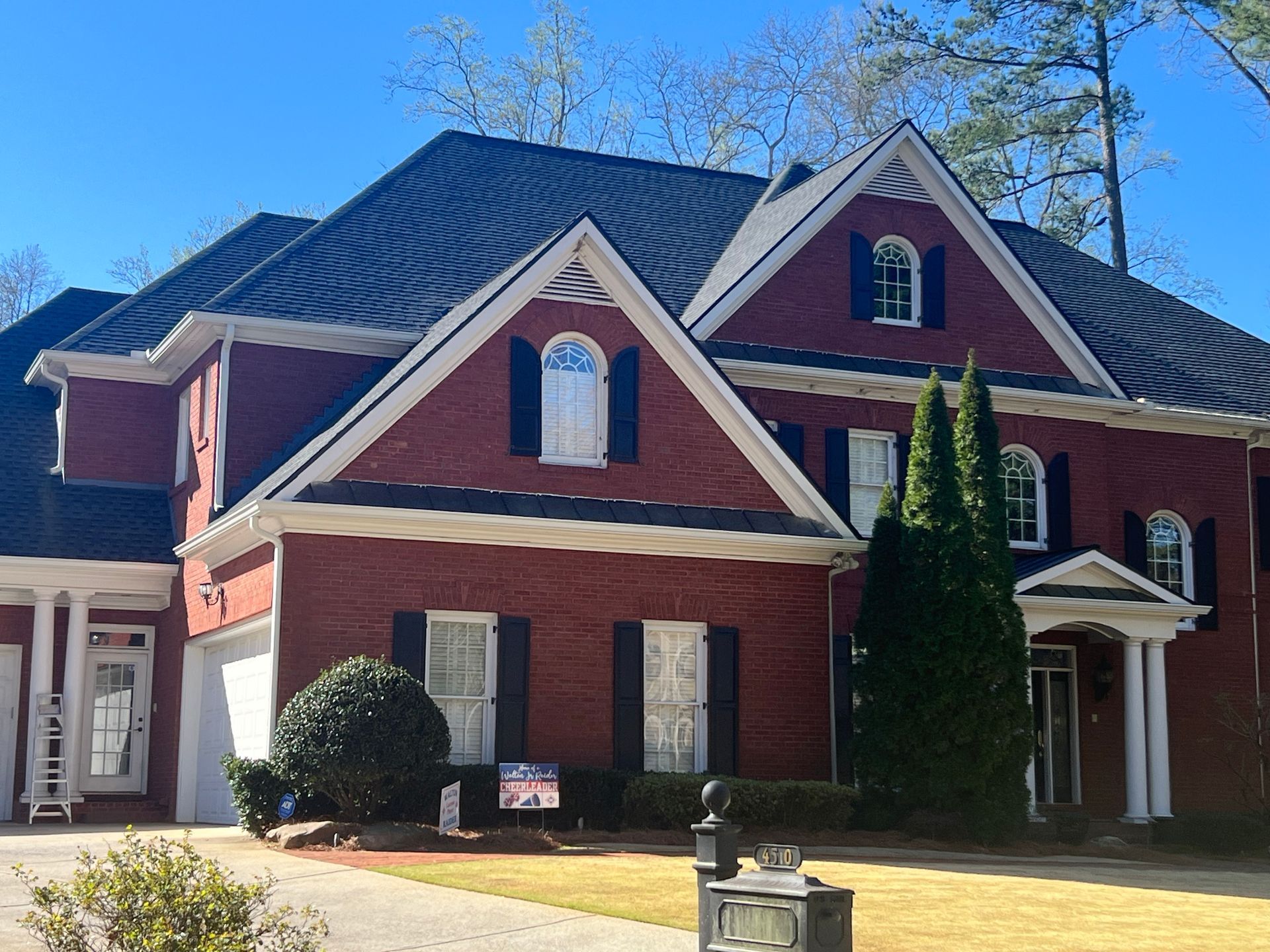 Red brick house with dark roof and white trim under a clear blue sky.
