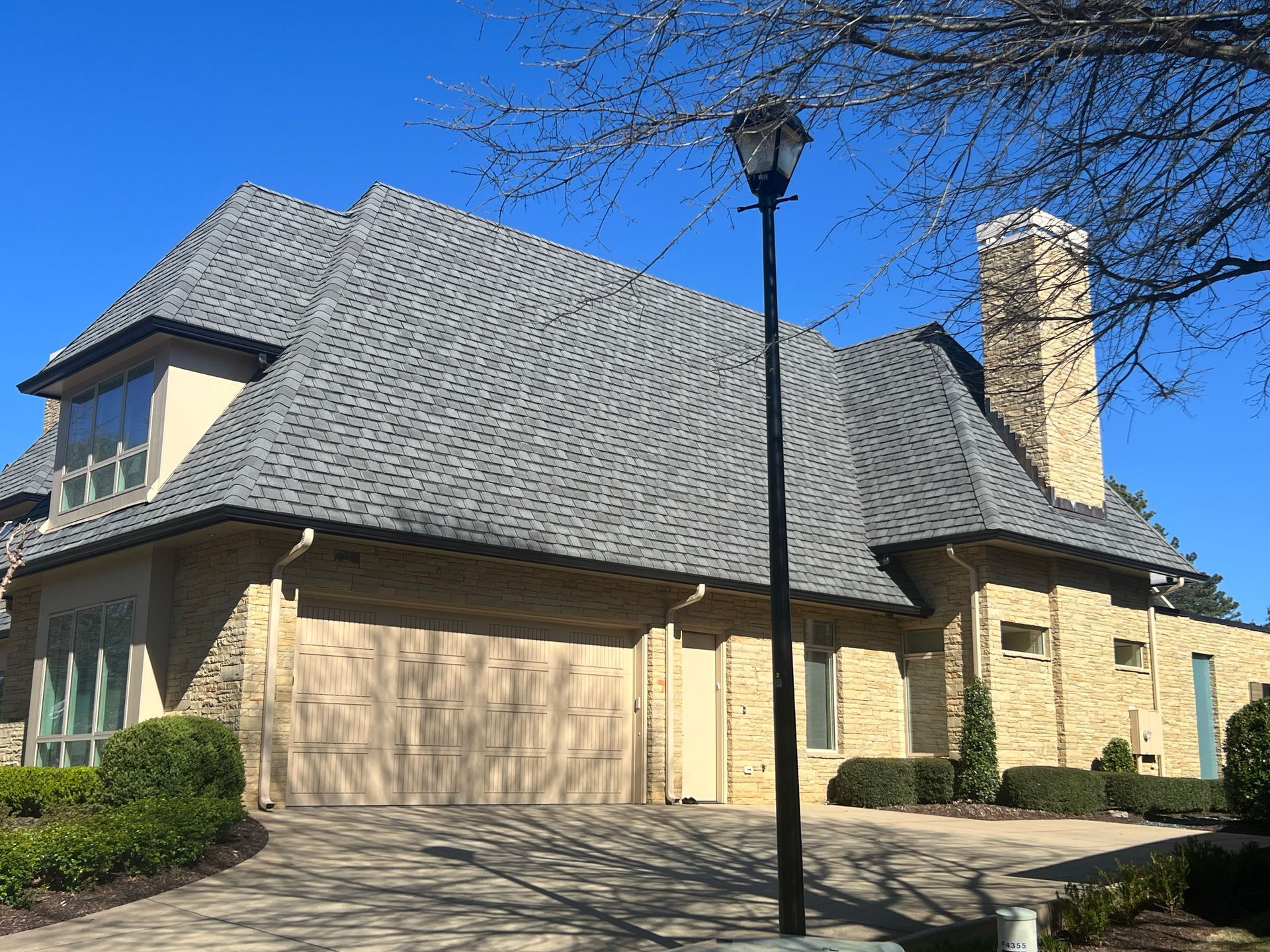 Beige brick house with gray roof and a tall chimney under a blue sky.
