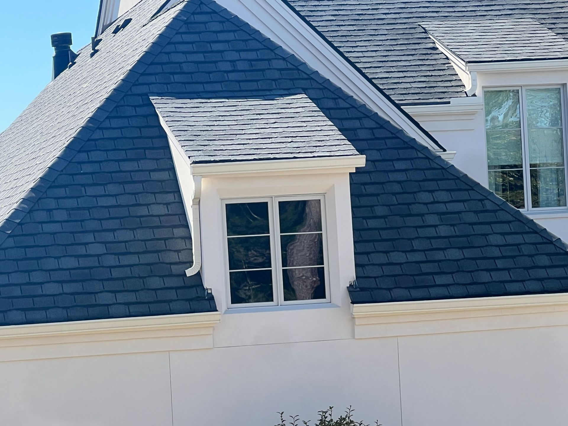 A white building with a dark gray shingled roof and a dormer window.