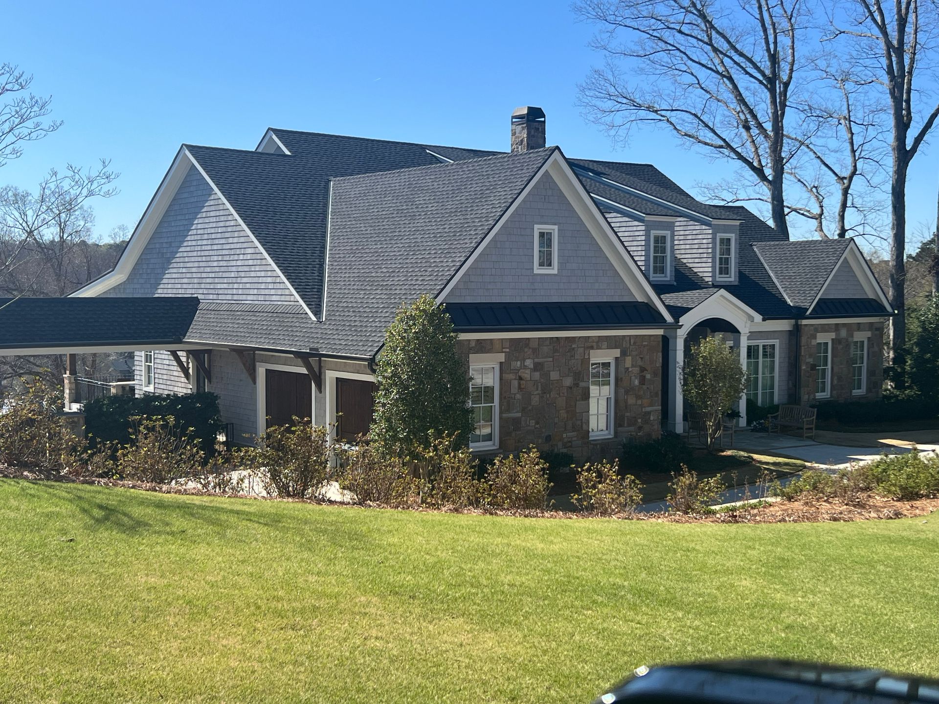 Blue and gray house with multiple rooflines, a stone facade, and a grassy lawn on a sunny day.