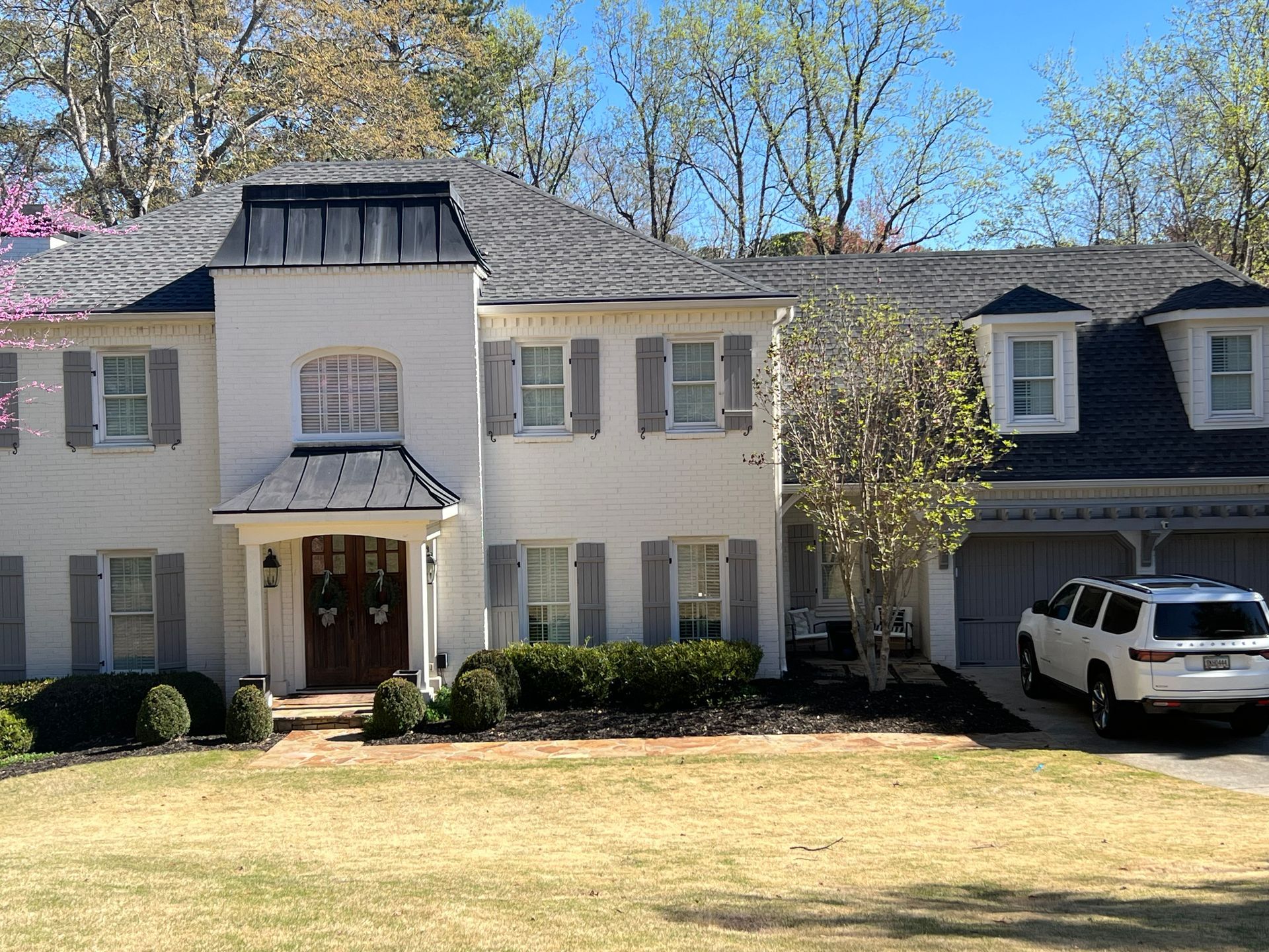 White two-story house with gray shutters and roof. A white SUV is parked in the driveway.