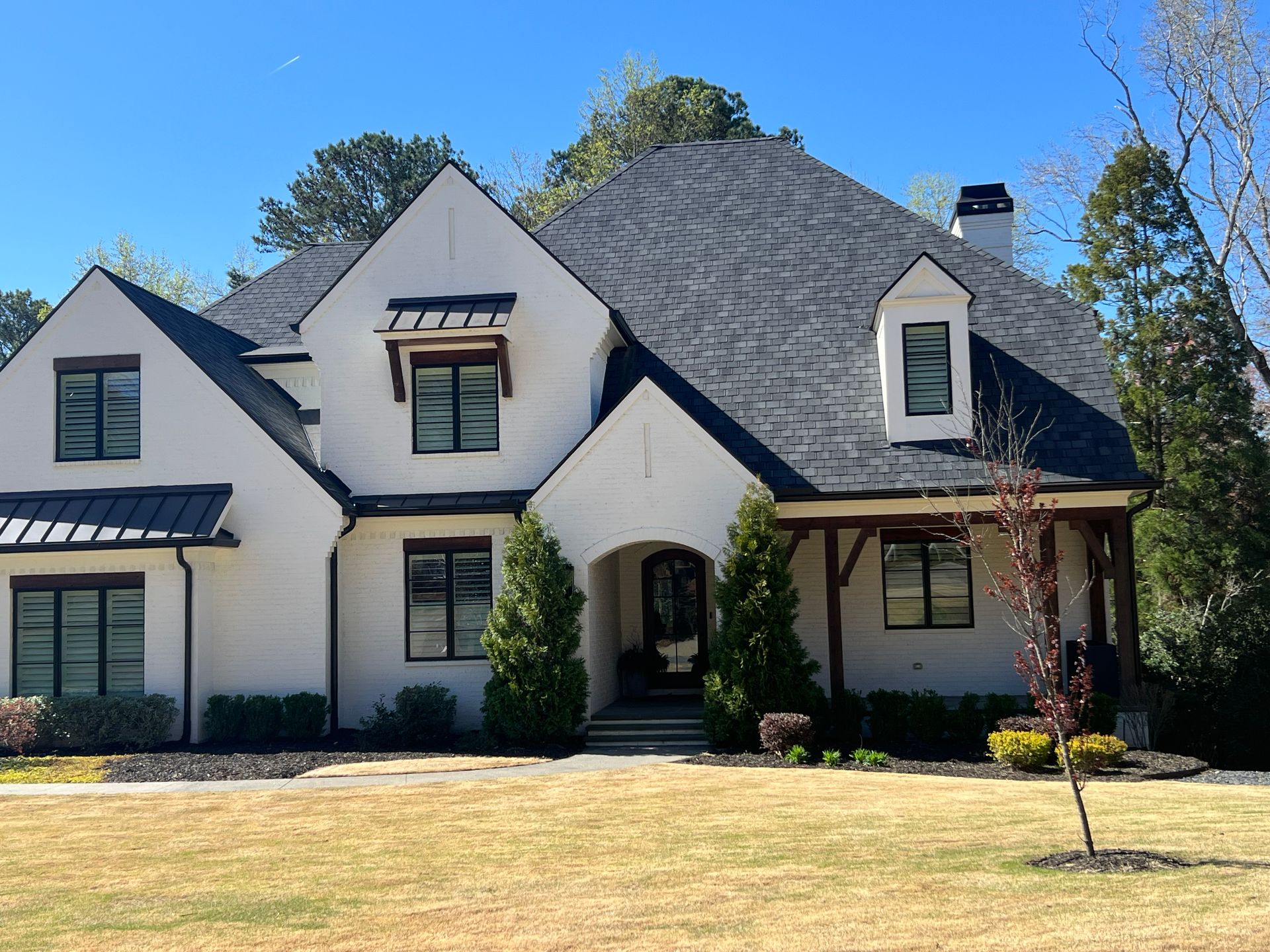 White house with black roof and trim, arched doorway, and small evergreen trees.