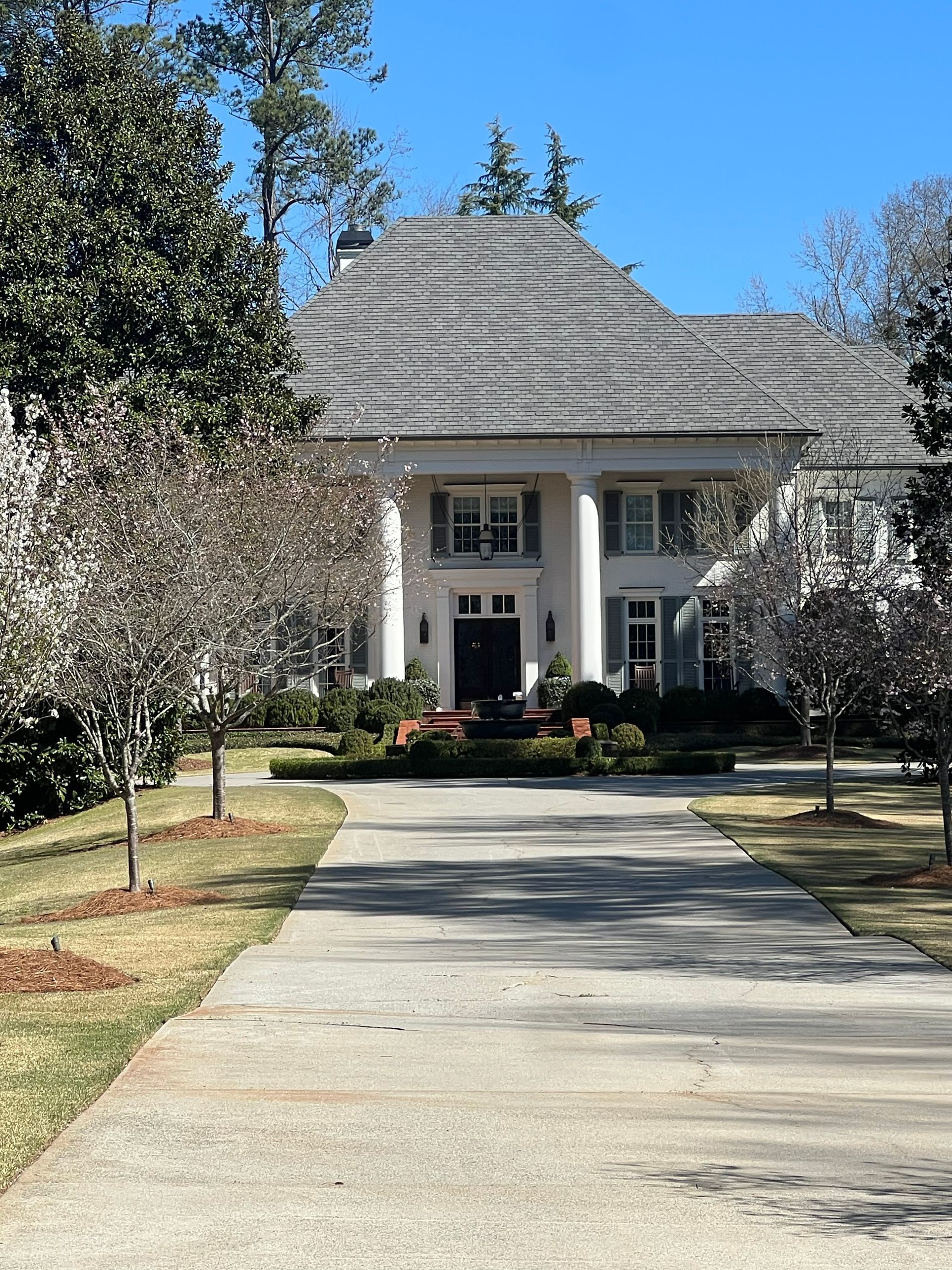 White mansion with columns, driveway, and trees under a clear blue sky.