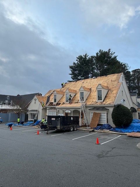 Roofers working on a building with a newly exposed wooden roof. Tarps cover the ground. Cloudy sky.