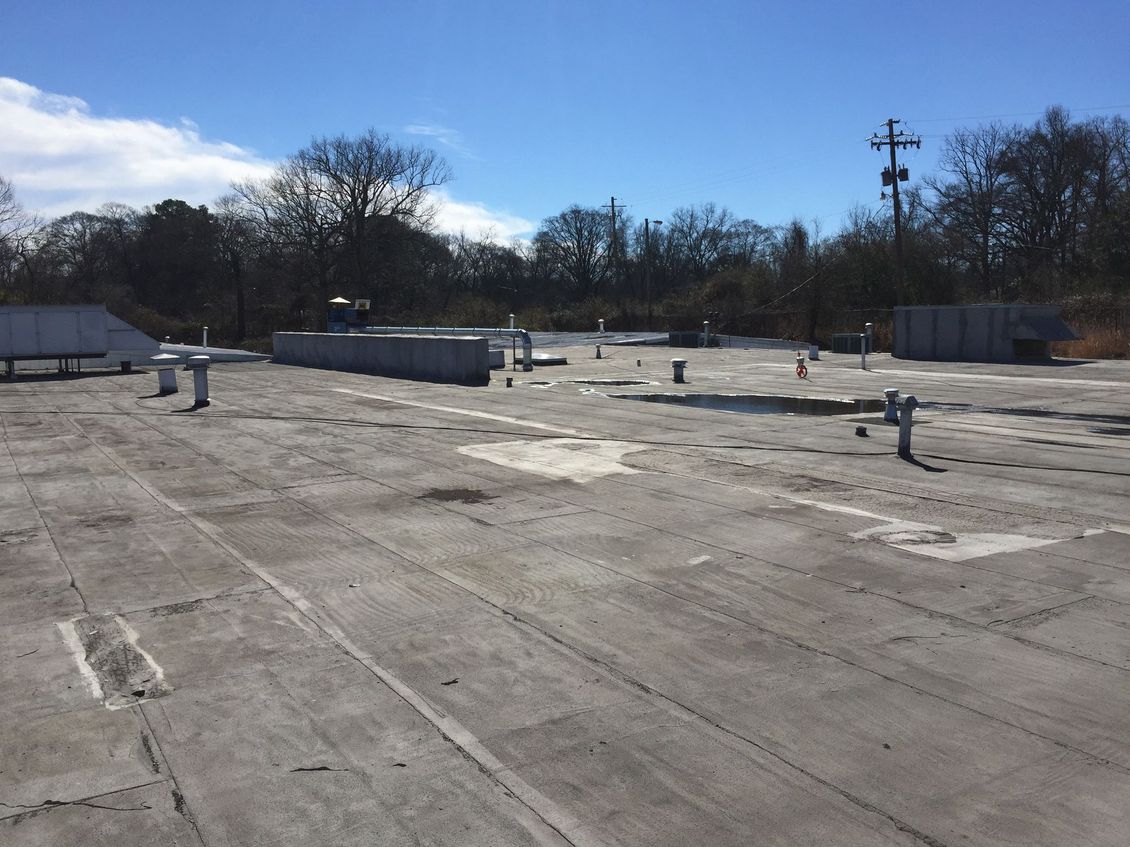 Flat, light gray commercial rooftop with vents and equipment against a clear, sunny sky.