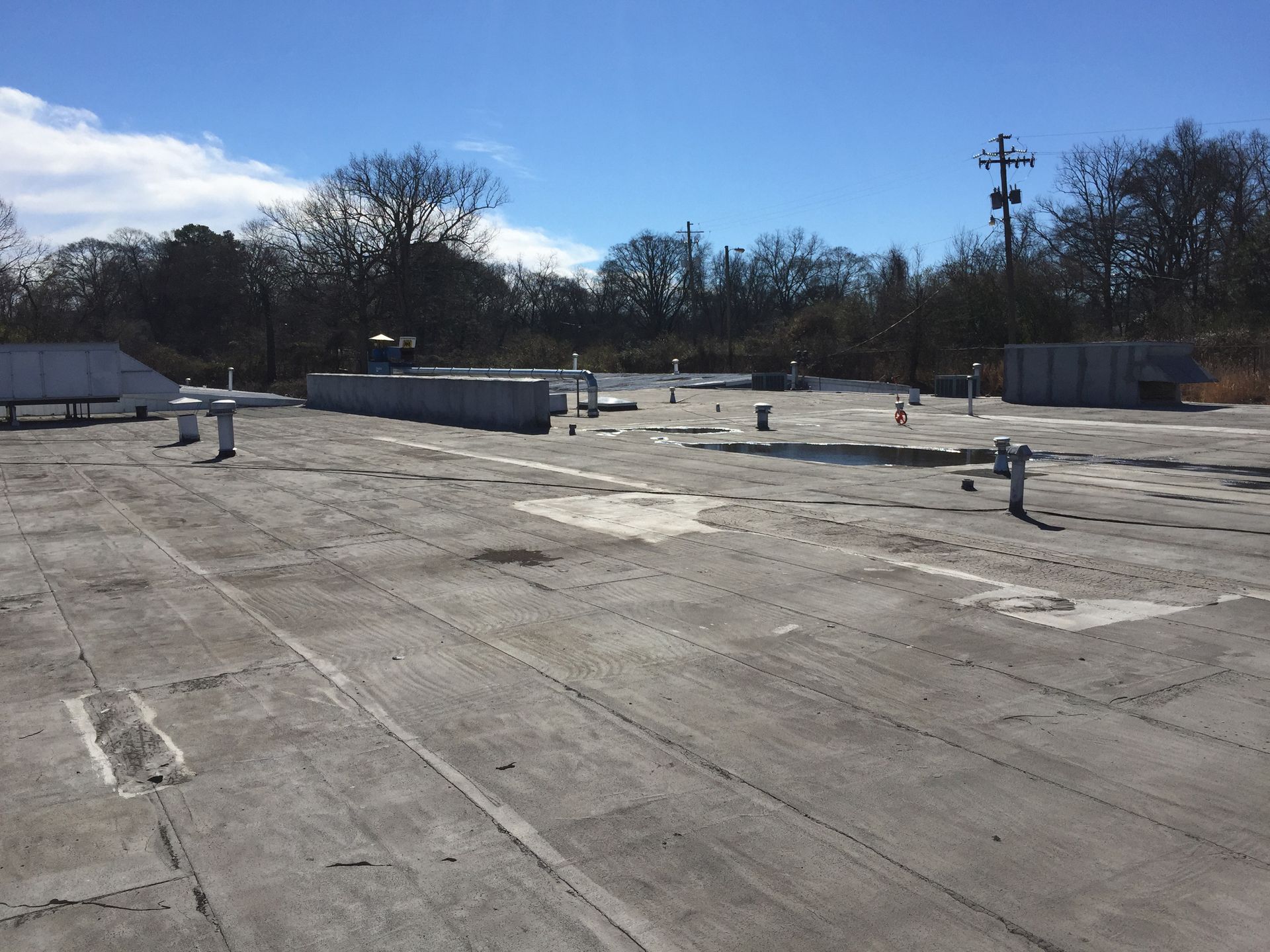 Flat, weathered commercial rooftop with various pipes and equipment, sunny day.
