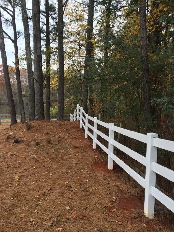White fence along a wooded path covered in brown pine needles in autumn