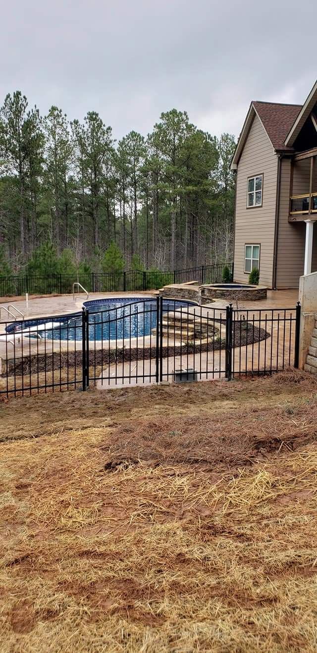 Backyard with fenced-in swimming pool beside a brick house, surrounded by trees and dry grass.