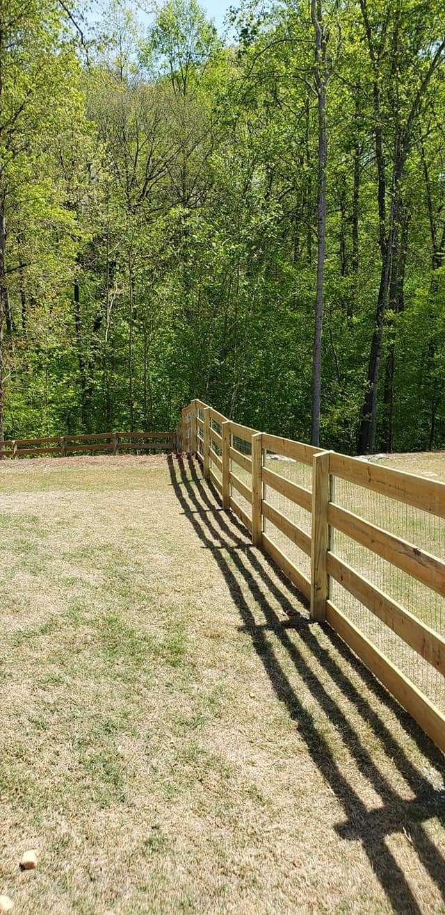 Wooden fence bordering a grassy yard beside a leafy green forest