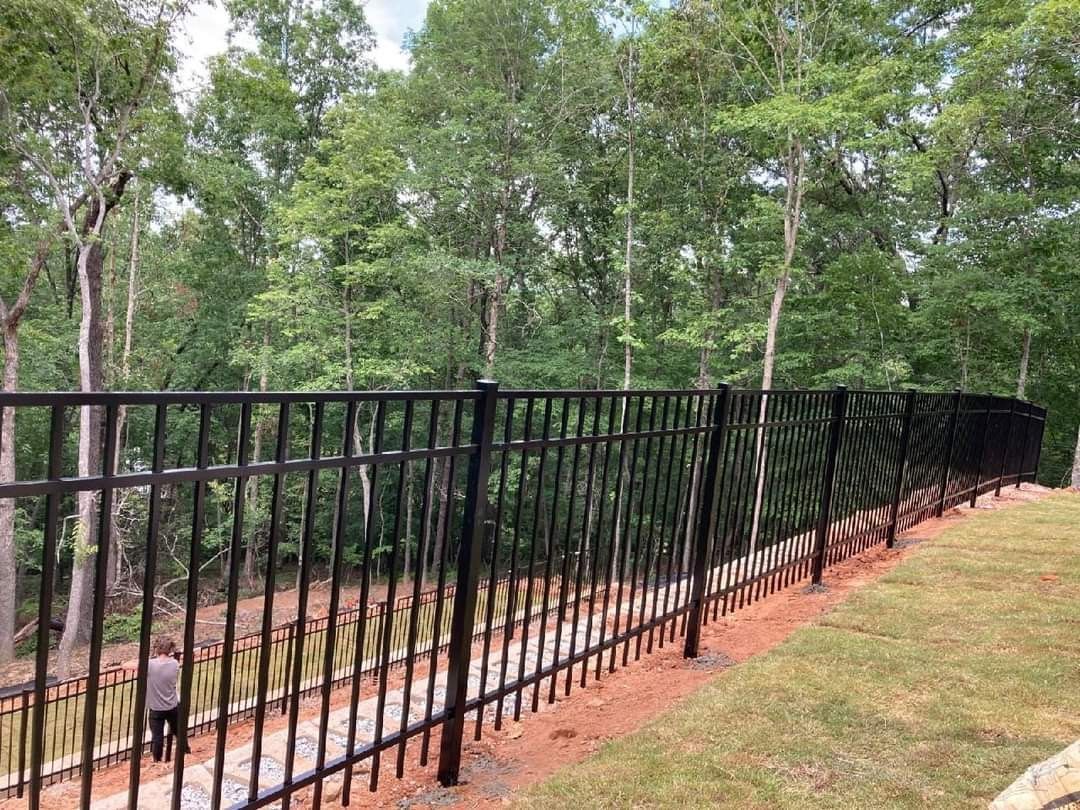 Black metal fence along a grassy path beside a wooded area