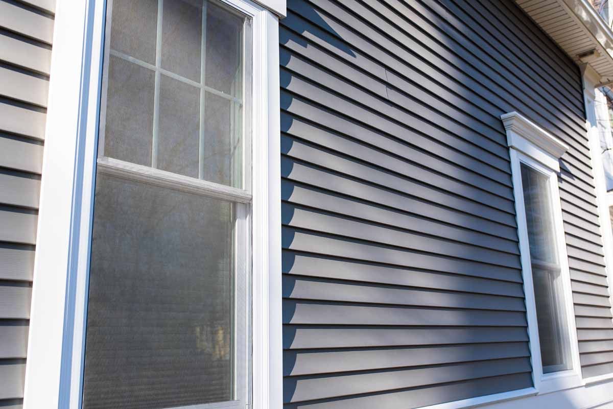 Gray siding on a house with white window frames.