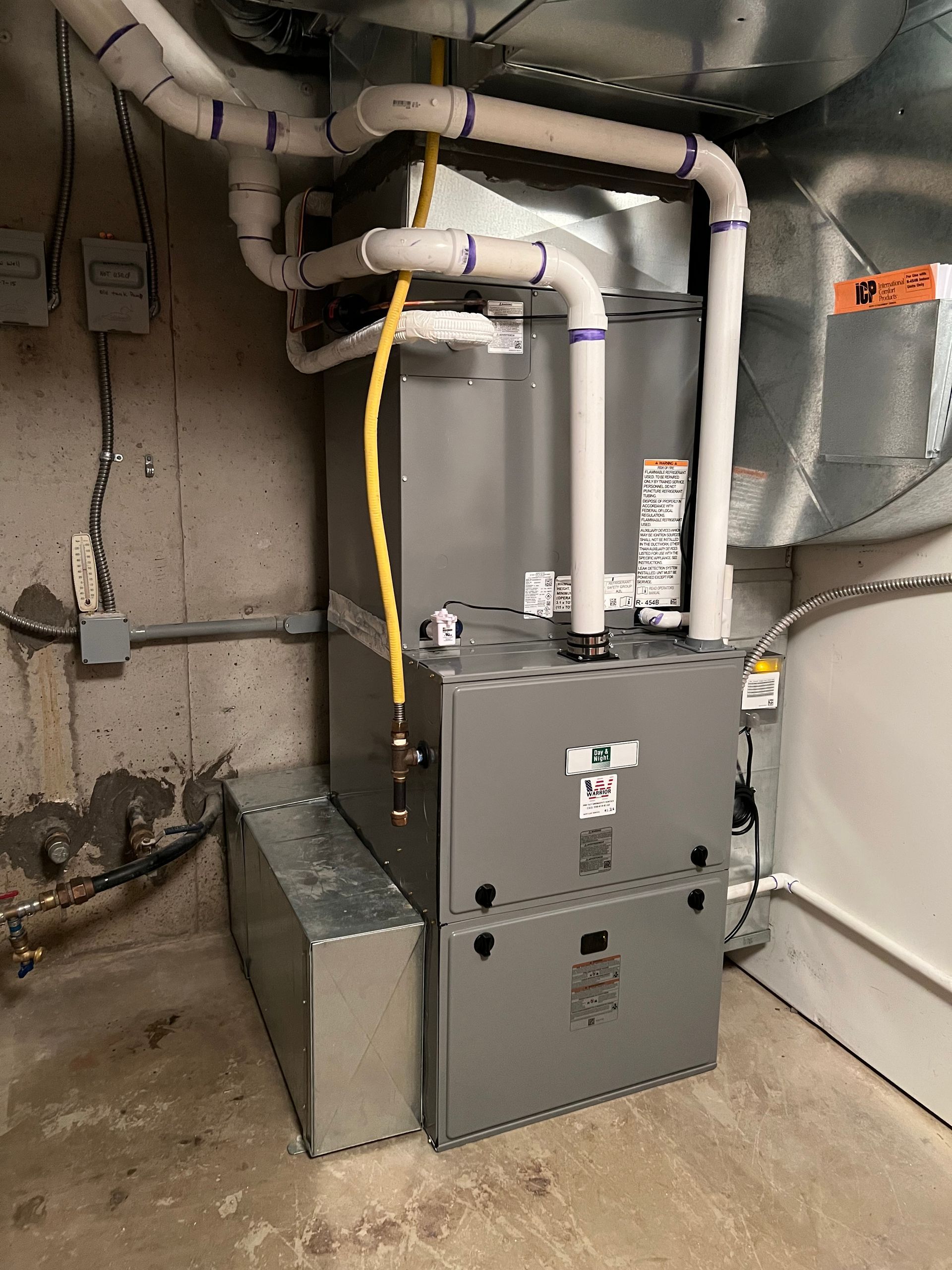 A furnace unit with ducts and piping in a basement setting. Gray and white colors dominate.