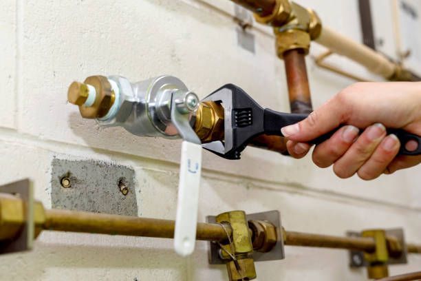 Hand holding a wrench, tightening a fitting on copper pipes in a mechanical room.