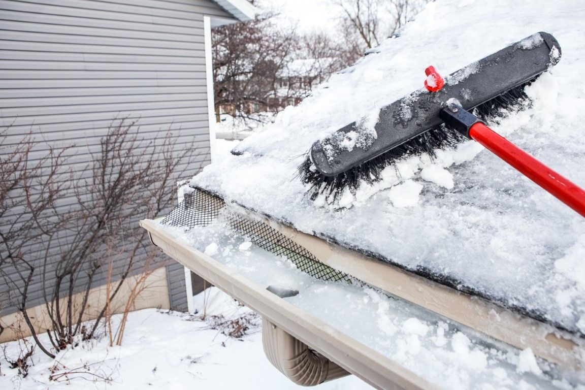Person clearing snow from a roof with a red rake near a house siding