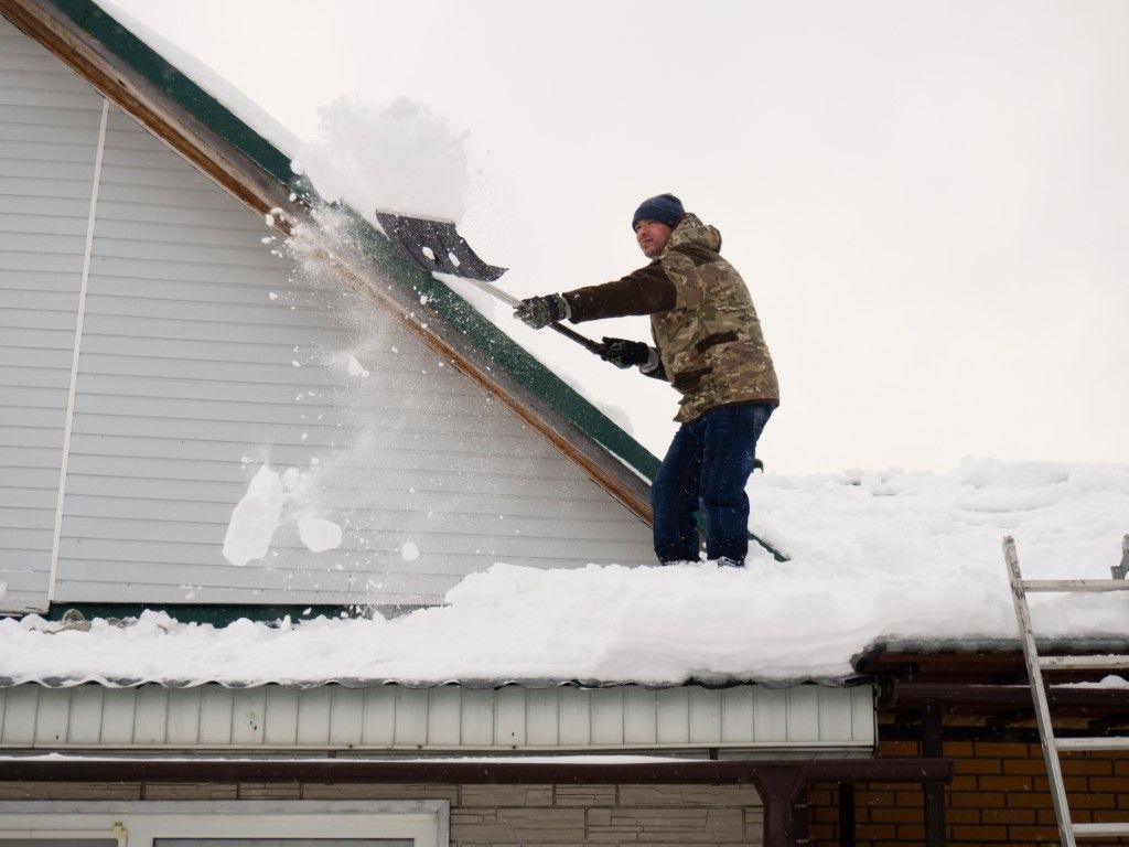 Person shoveling snow off a steep roof in a snowy outdoor setting