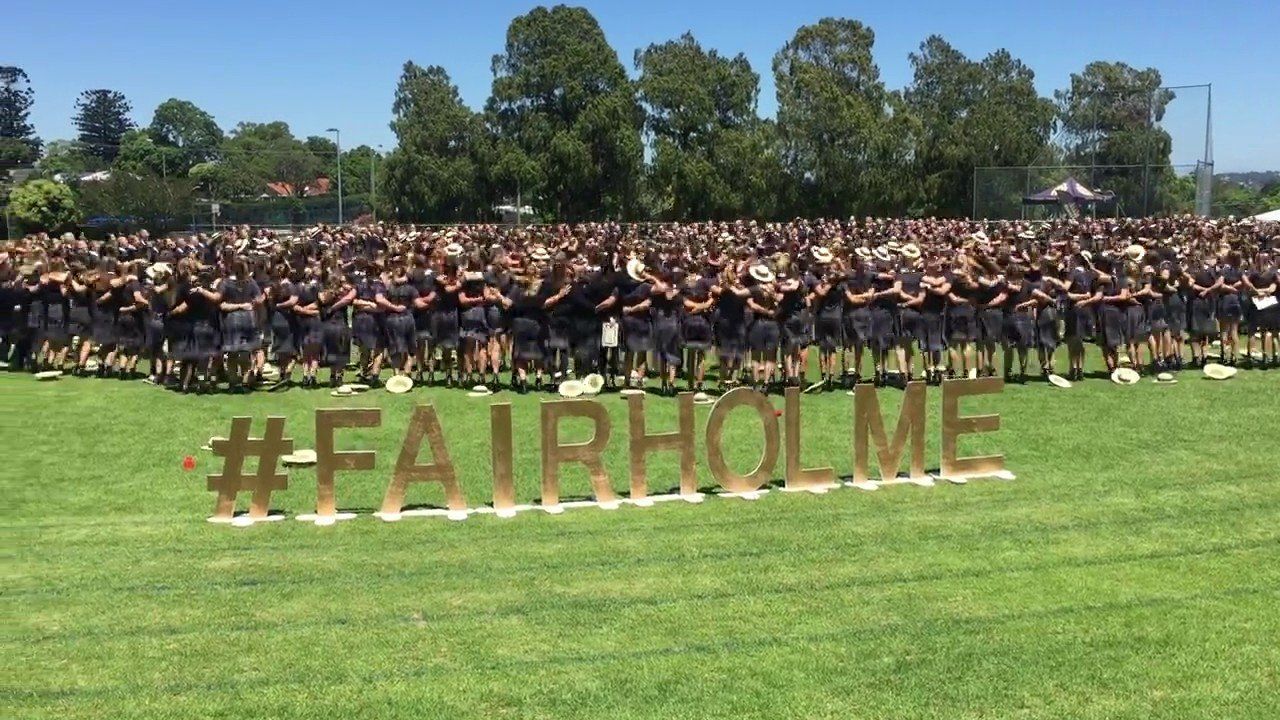 A large group of people are standing in a field with the word fairholme written in gold letters