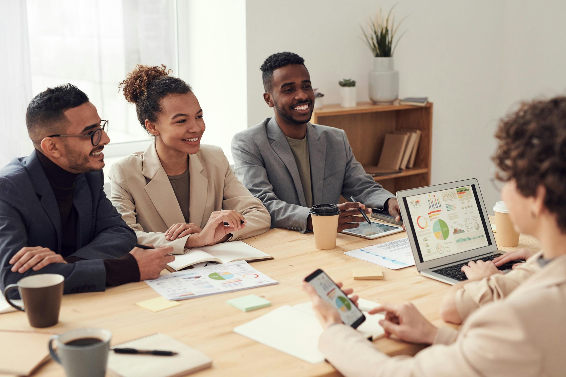 People in a business meeting at a table, looking at a laptop and documents, smiling.