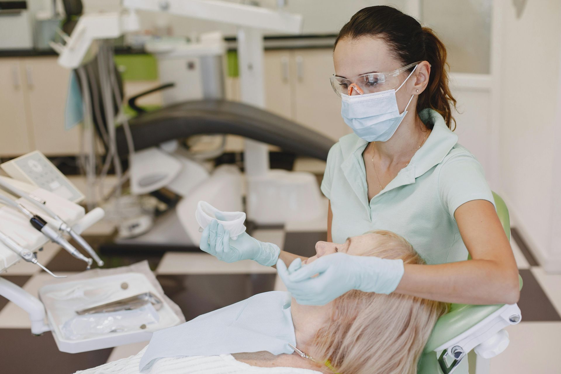 Dentist with mask and gloves examining a patient's mouth in a dental office.