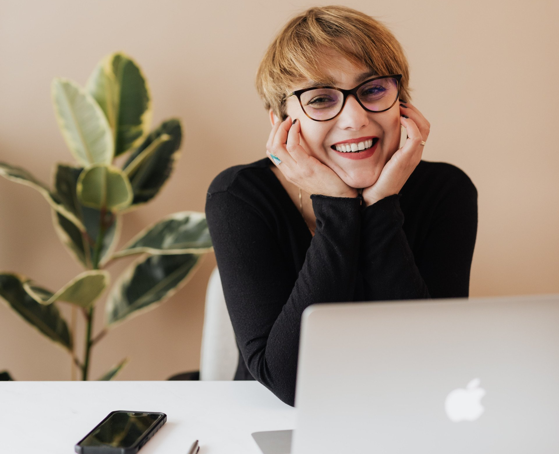 young smiling woman sitting at a desk with mobile phone and laptop next to her