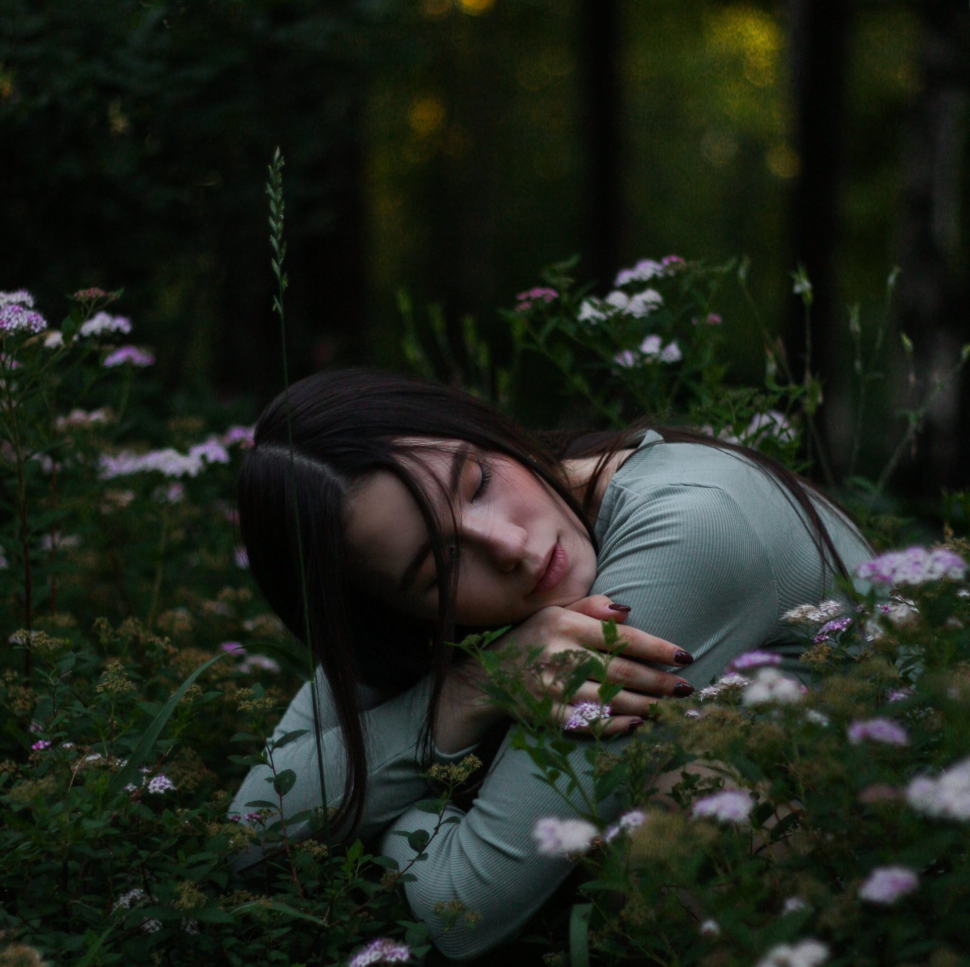 young woman sitting on the floor with her head on her knees in lush green garden