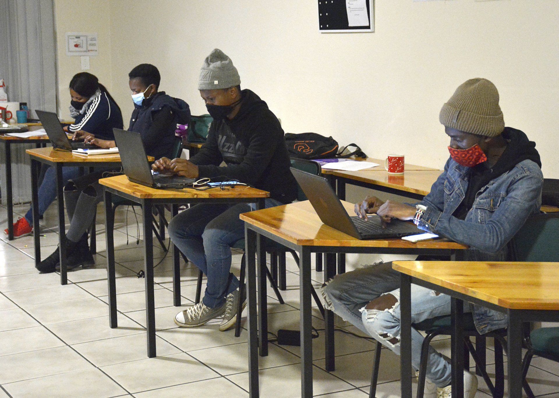 four students sitting at desks working on laptops