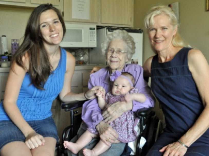 Three women are posing for a picture with an elderly woman in a wheelchair holding a baby